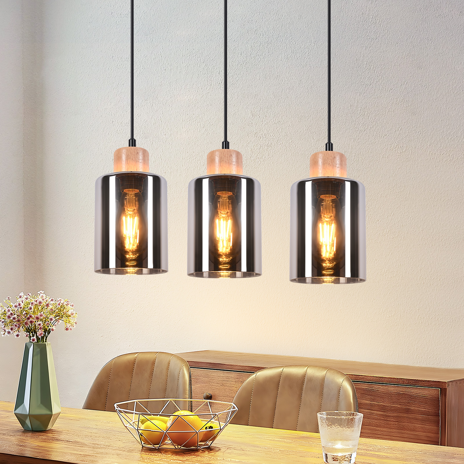 Drei Pendelleuchten mit Holzaufsätzen hängen über einem Tisch. Eine Blumenvase, eine Obstschale, Stühle und ein Schrank sind ebenfalls sichtbar.