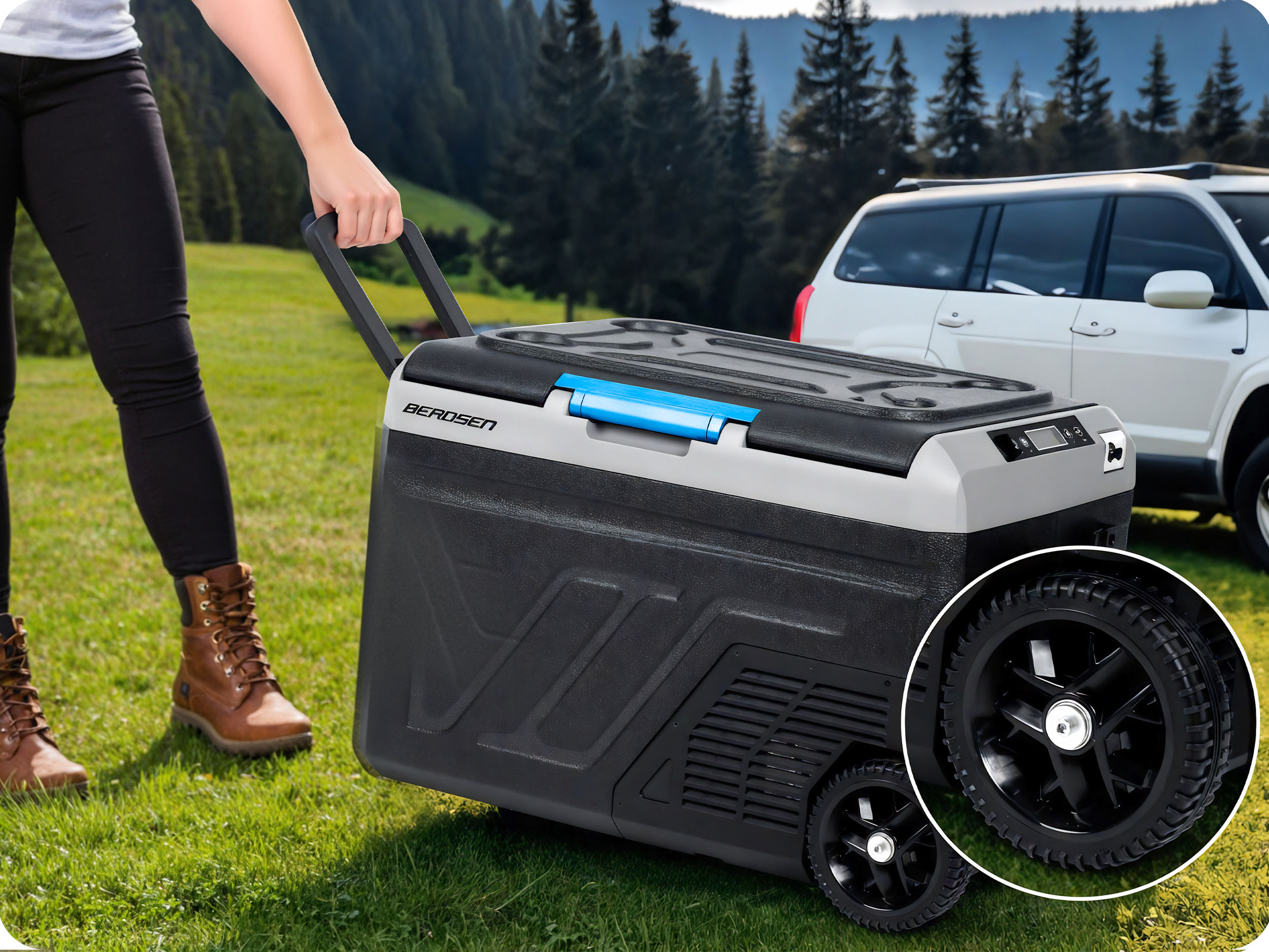Osoba ciągnie czarną chłodziarkę na kółkach po trawie. Biały SUV w tle, widoczne drzewa.