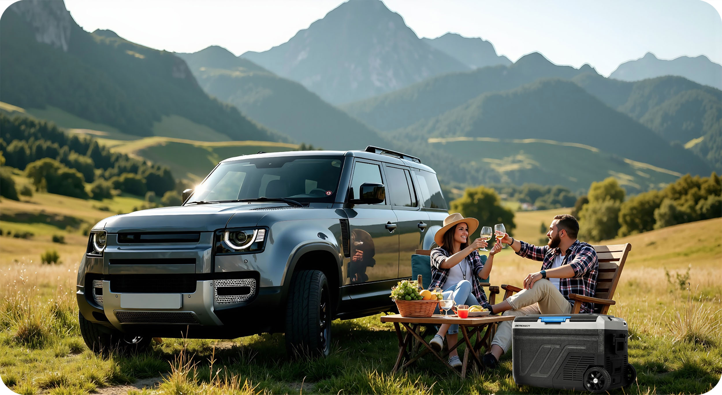 Para wznosi toasty kieliszkami wina w pobliżu szarego SUV-a w górskim krajobrazie. W pobliżu stoi lodówka.