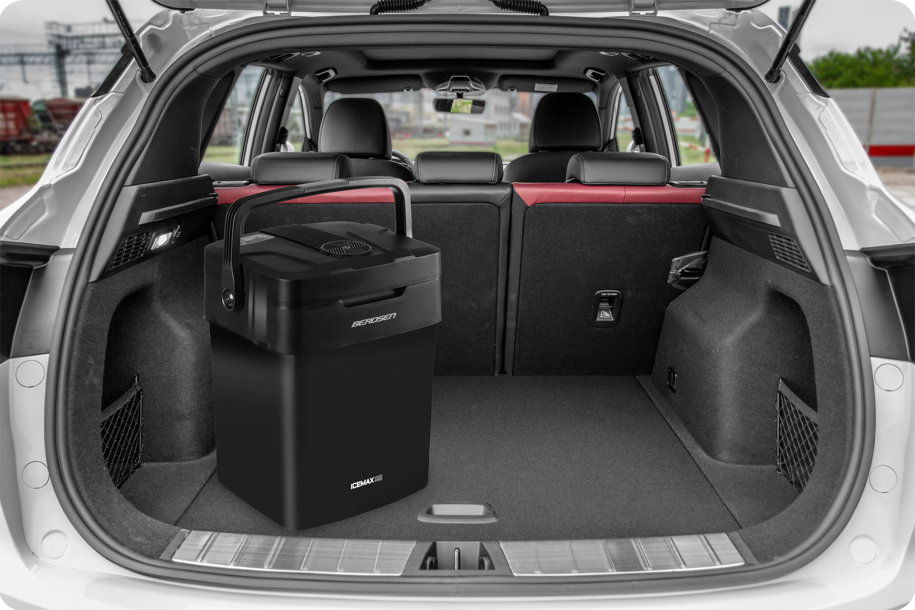 Otwarty bagażnik samochodu z czarną lodówką. Tło pokazuje siedzenia samochodowe i otoczenie.