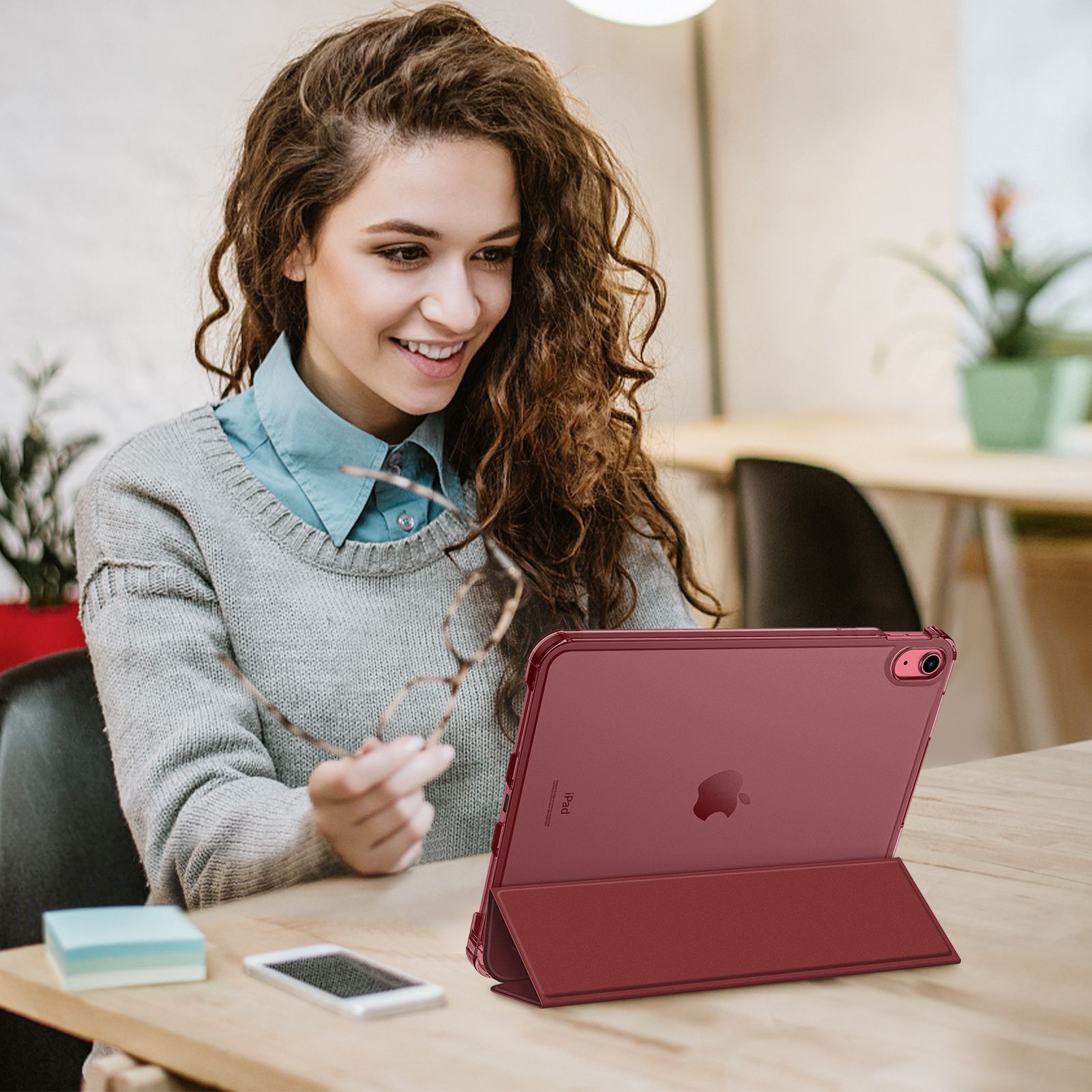 Eine Frau lächelt einen Tablet-PC an. Sie hält eine Brille. Das Tablet steht auf einem Schreibtisch.