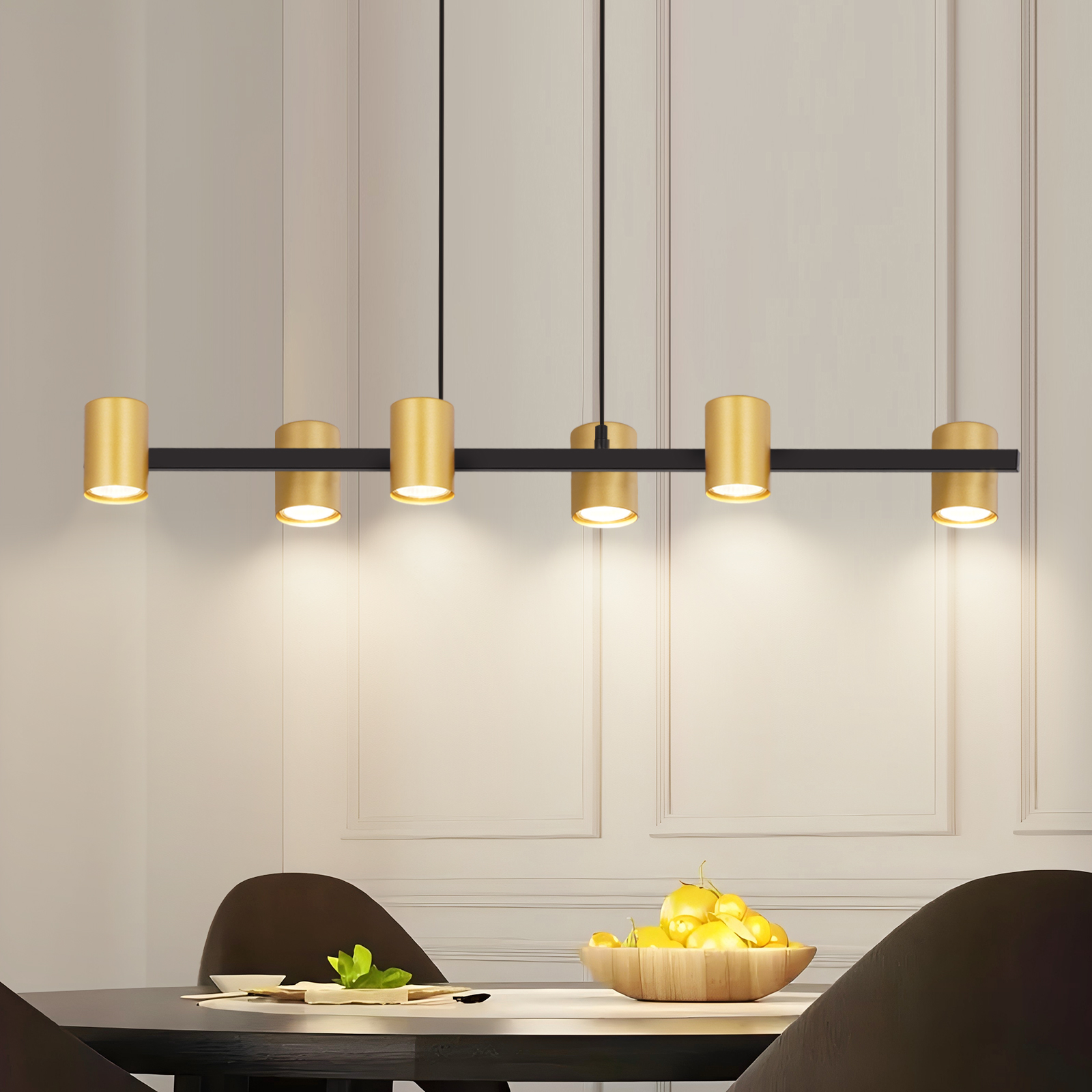Ein modernes Esszimmer mit einem gold-schwarzen Kronleuchter. Eine Holzschale mit Zitronen steht auf dem Tisch.