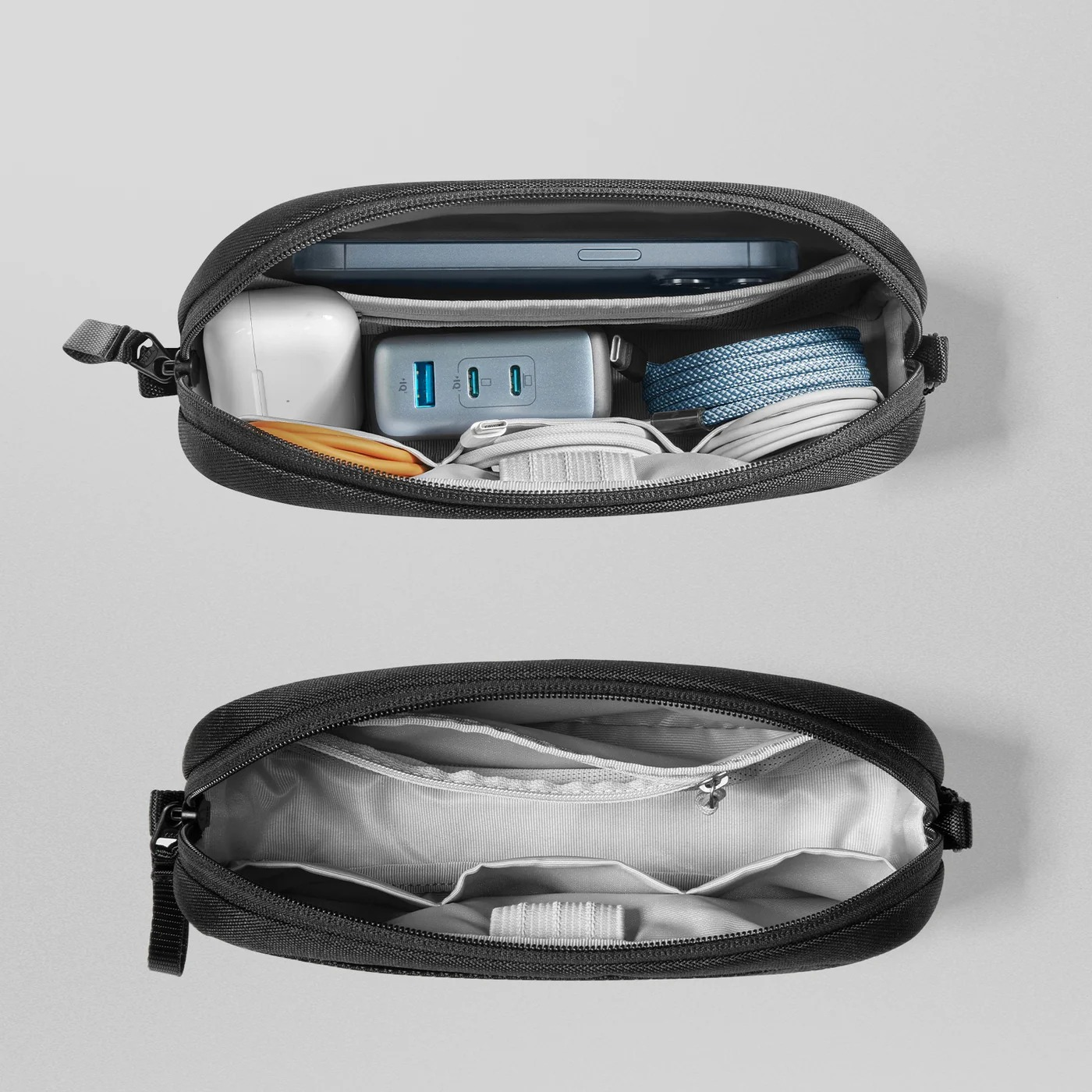 Schwarze Tasche mit Tech-Zubehör: Telefon, Ladegerät, Ohrhörer und Kabel. Unten eine leere Tasche mit Taschen.