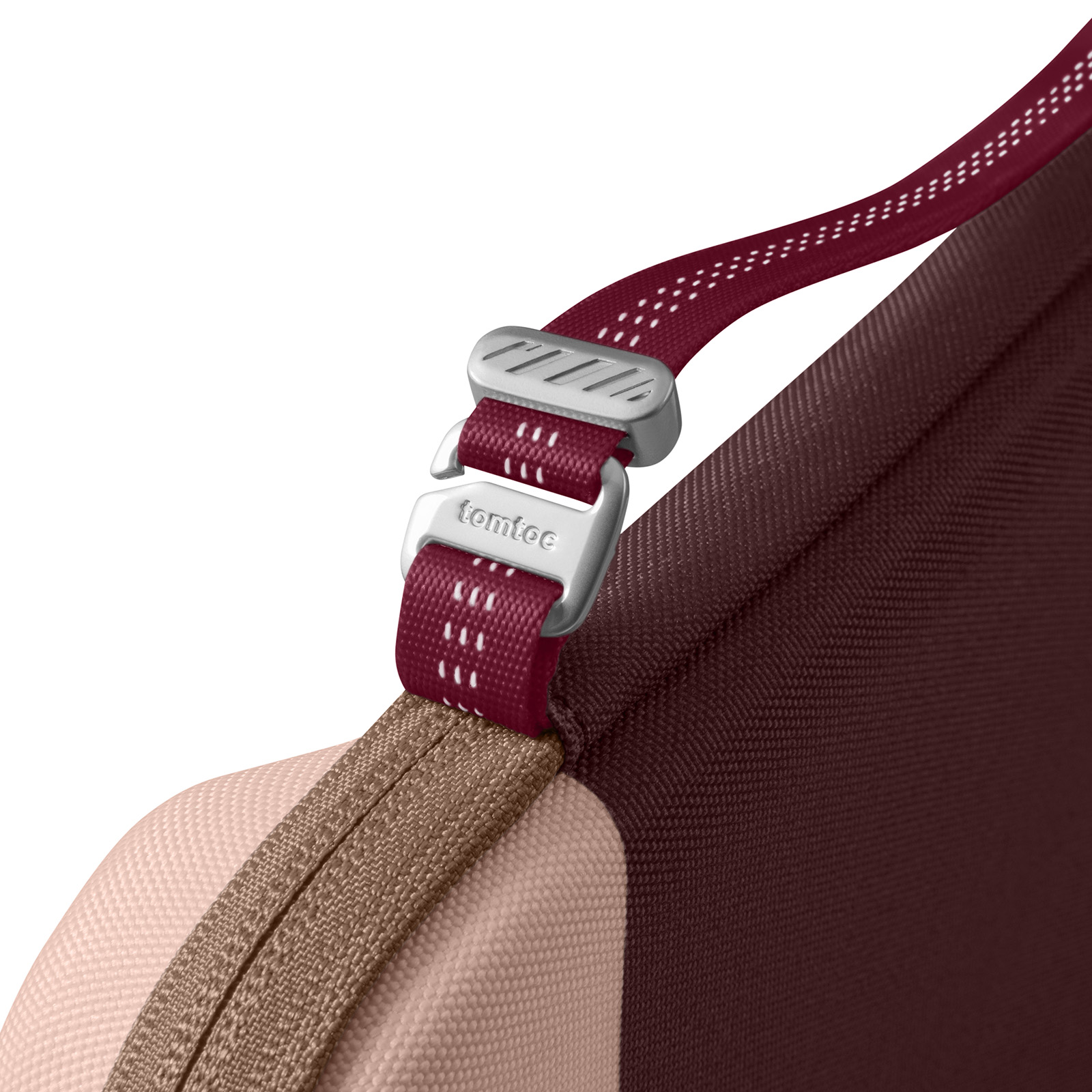 Zbliżenie torby z paskiem i metalową klamrą. Pasek jest bordowy z białymi przeszyciami, torba ma ciemnoczerwony kolor.