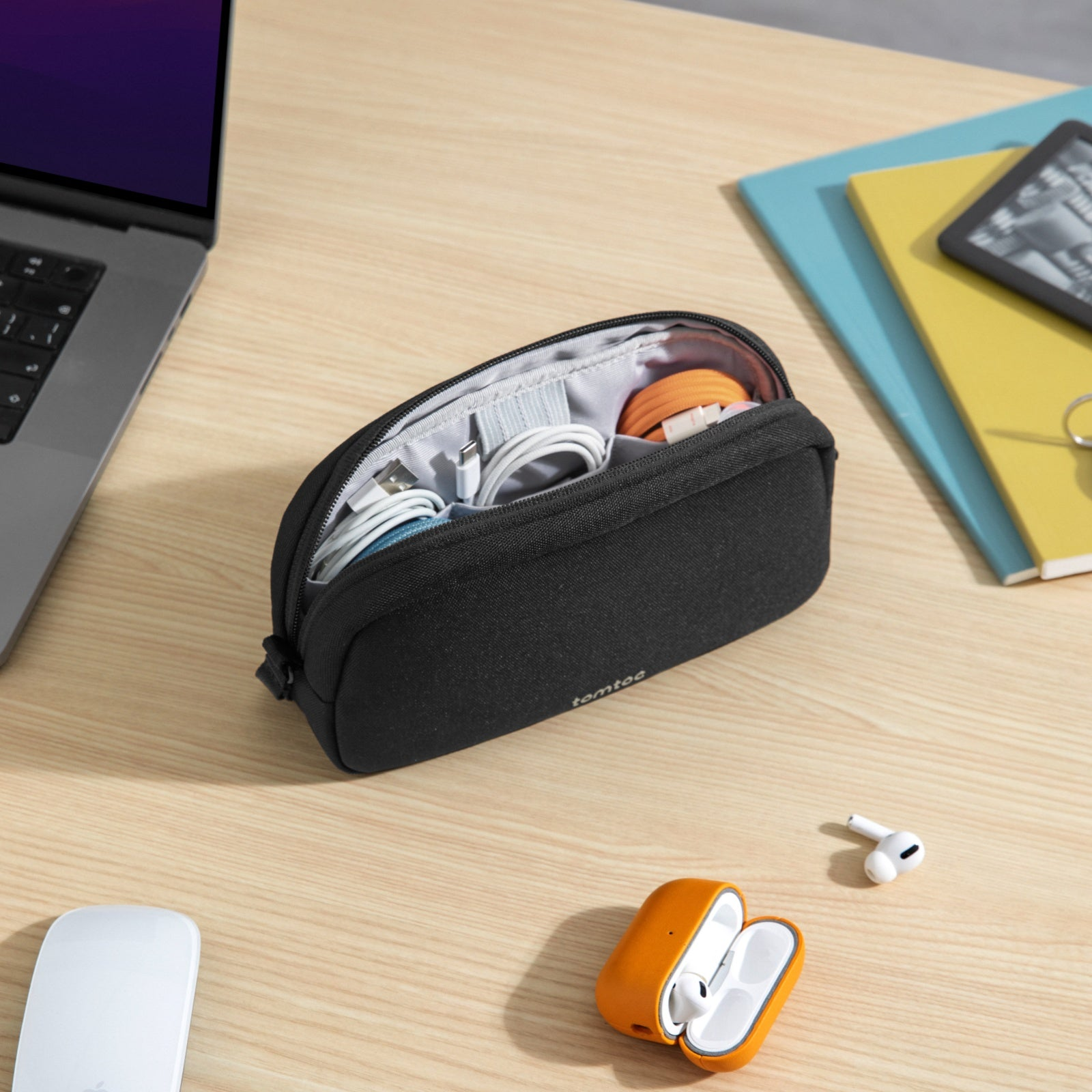 Schwarzes Federmäppchen mit Kabeln. Orangefarbene AirPods-Hülle, AirPods, Laptop, Maus und Notizbücher auf einem Holztisch.