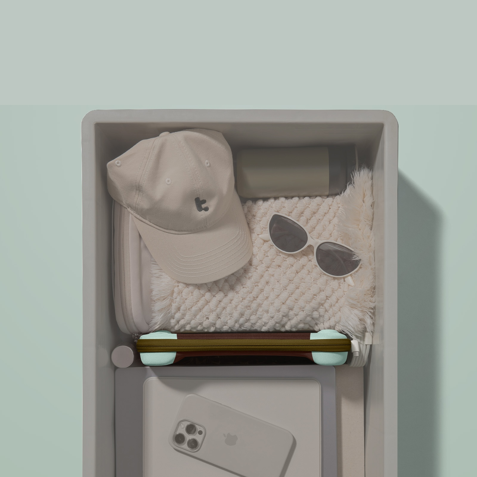 Szuflada zawiera czapkę, okulary przeciwsłoneczne, koc i telefon. Szuflada jest biała, na miętowo-zielonym tle.