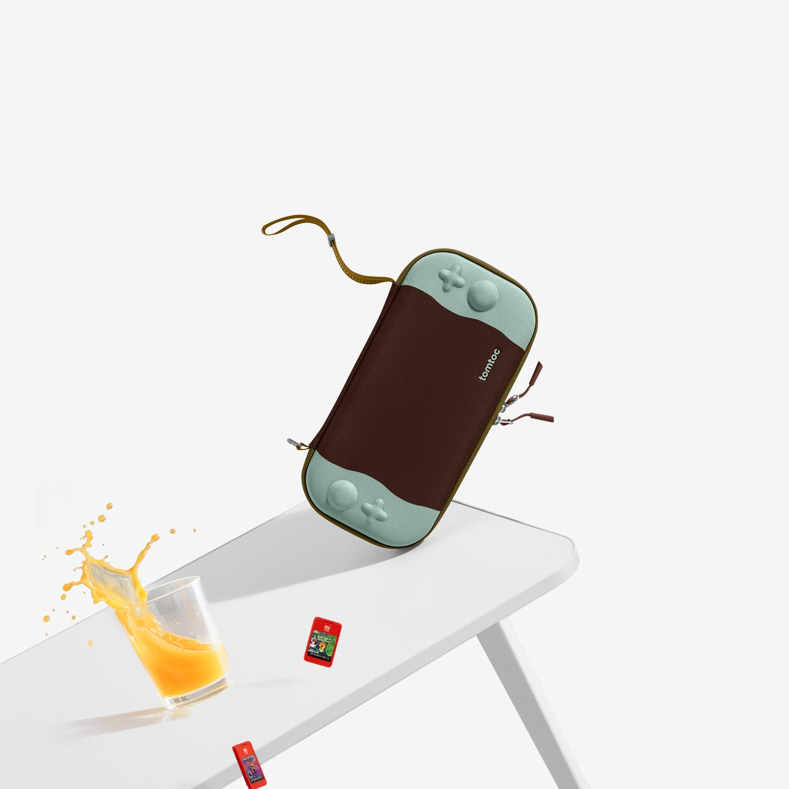 Etui na Switch w powietrzu. Szklanka soku pomarańczowego się rozlewa. Kartridże do gier na białym stole.