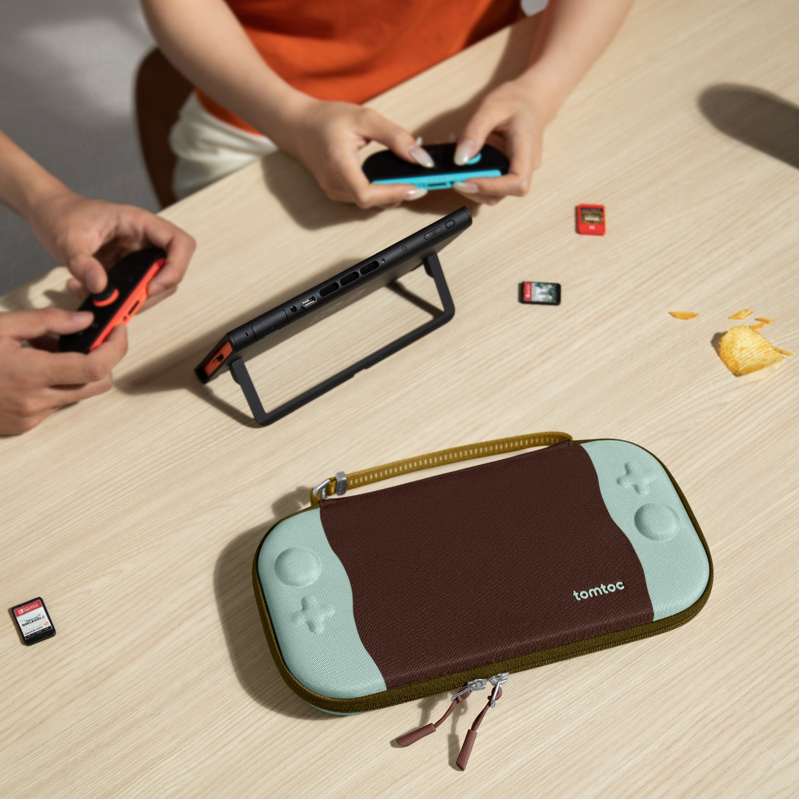 Ludzie grają w Switch na drewnianym stole. Etui, karty do gier i chips są również na stole.