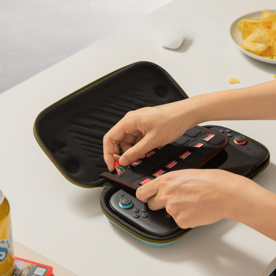 Dłonie umieszczają kartę do gry w etui Switch. Na stole chipsy i napój.