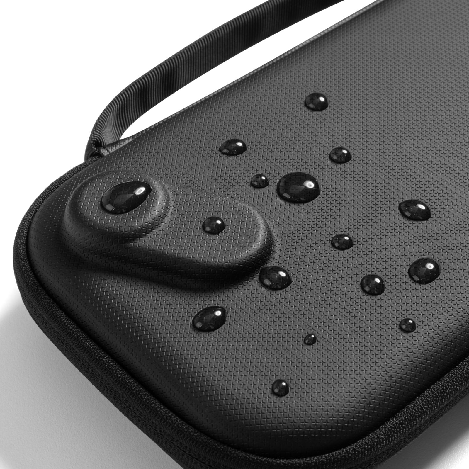 Czarny, teksturowany futerał z kroplami wody. Widoczny jest uchwyt. Futerał ma zaokrąglony kształt. Białe tło.