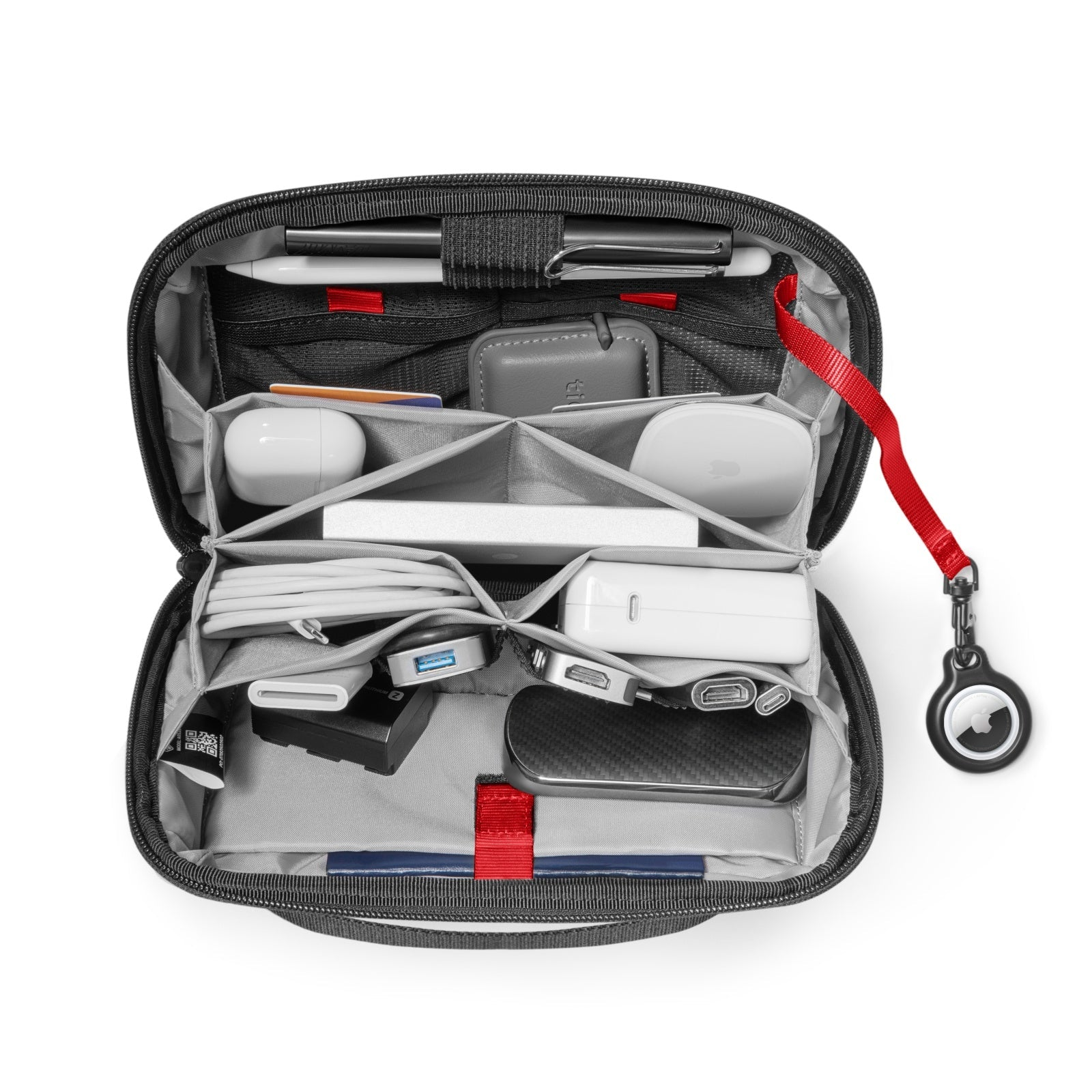 Otwarty czarny organizer technologiczny z różnymi gadżetami: długopis, ołówek, AirPods, ładowarka, kable i AirTag. Dołączony czerwony pasek.