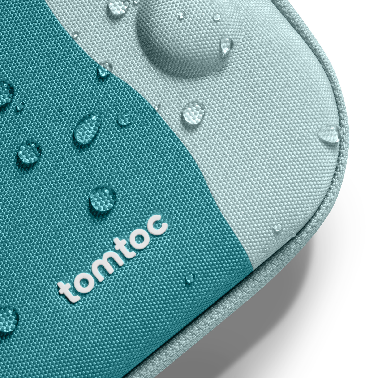 Zbliżenie na tkaninę w kolorze morskim i jasnoniebieskim z kroplami wody. Widoczna jest marka 'tomtoc'.