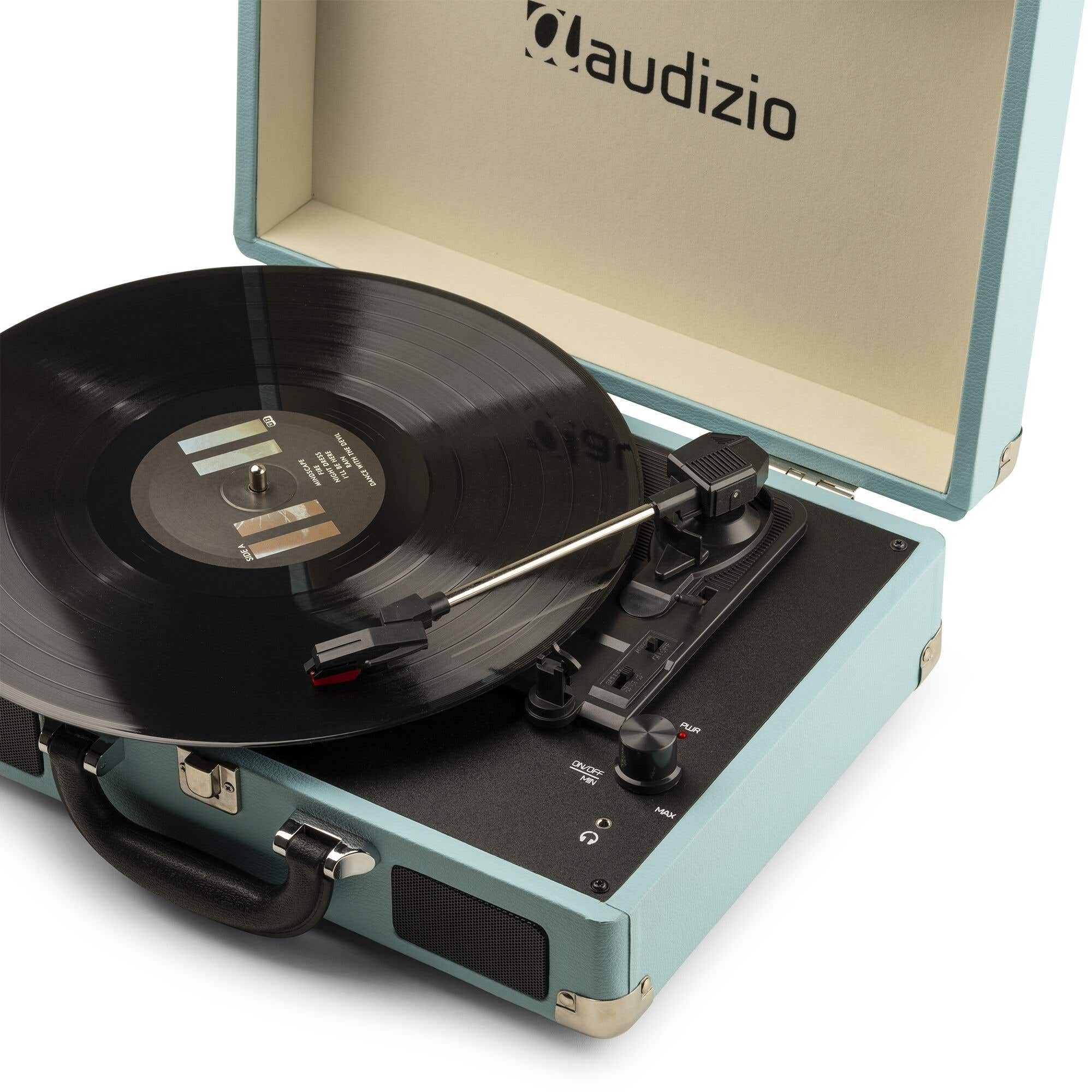 Un tocadiscos turquesa con un disco de vinilo negro. La tapa está abierta, mostrando el logo 'Maudizio'.