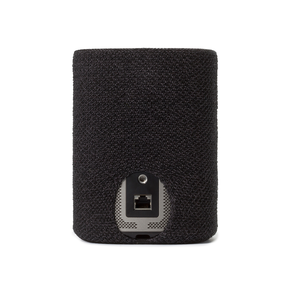 Un haut-parleur cylindrique noir avec une housse en tissu texturé. L'arrière a un port et un petit bouton circulaire.
