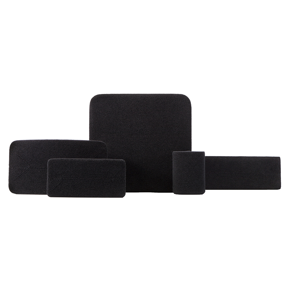 Plusieurs objets en tissu noir de formes et tailles variées sont disposés sur fond blanc. Ils semblent être des supports ou des coussinets.
