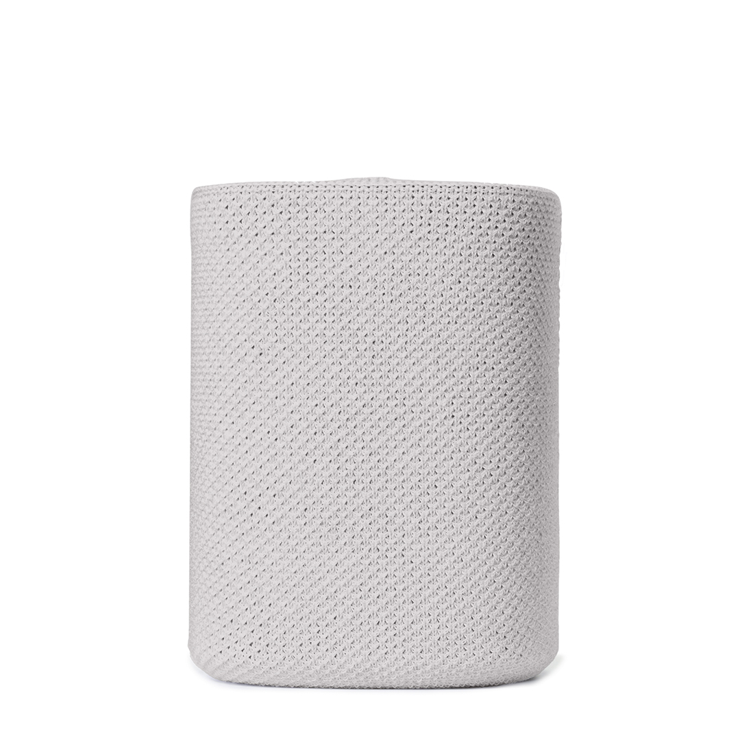 Un objet cylindrique en tricot gris clair se dresse sur fond blanc. La texture du tricot est visible.