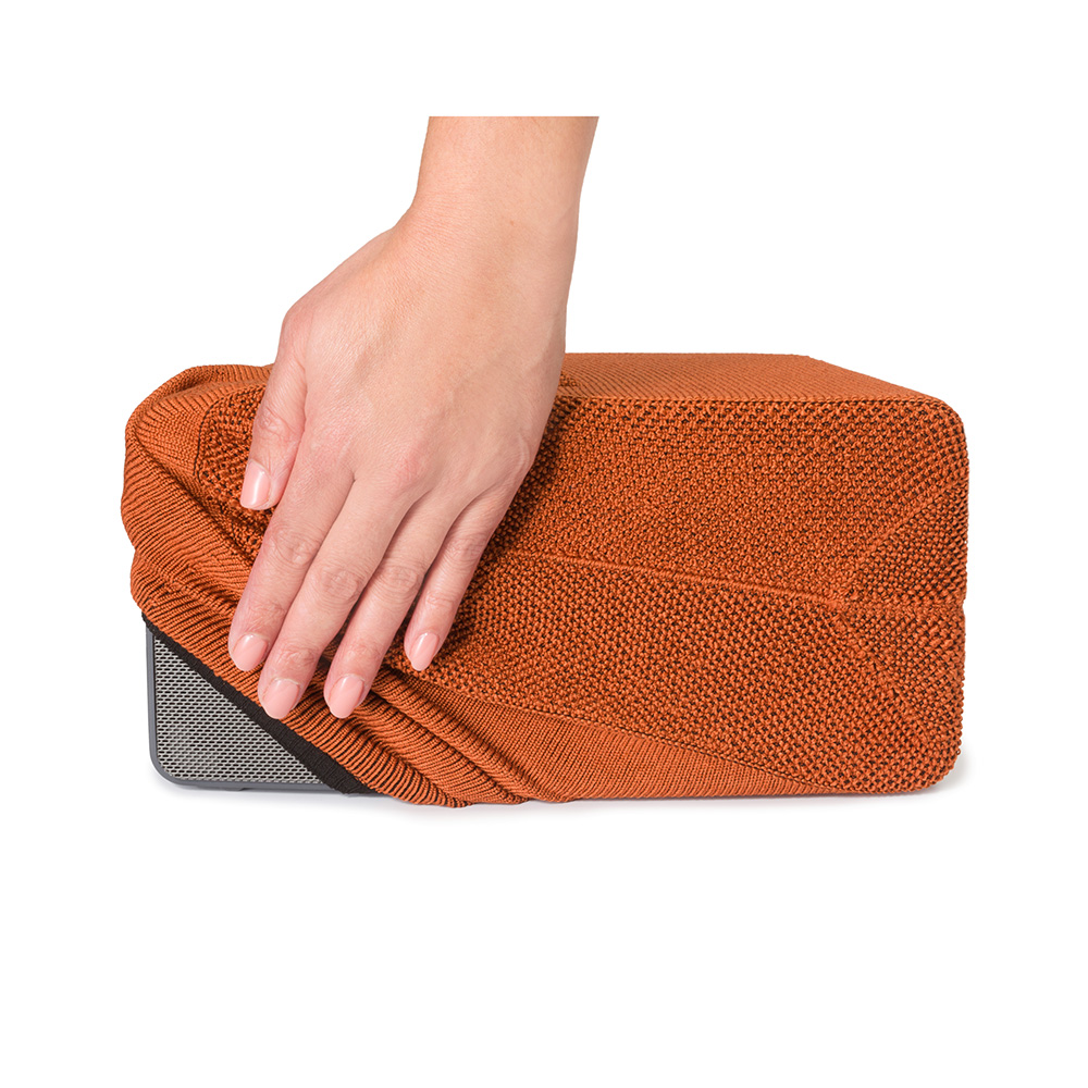 Eine Hand liegt auf einer rechteckigen, orangefarbenen Lautsprecherabdeckung. Der Lautsprecher ist dunkelgrau. Weißer Hintergrund.