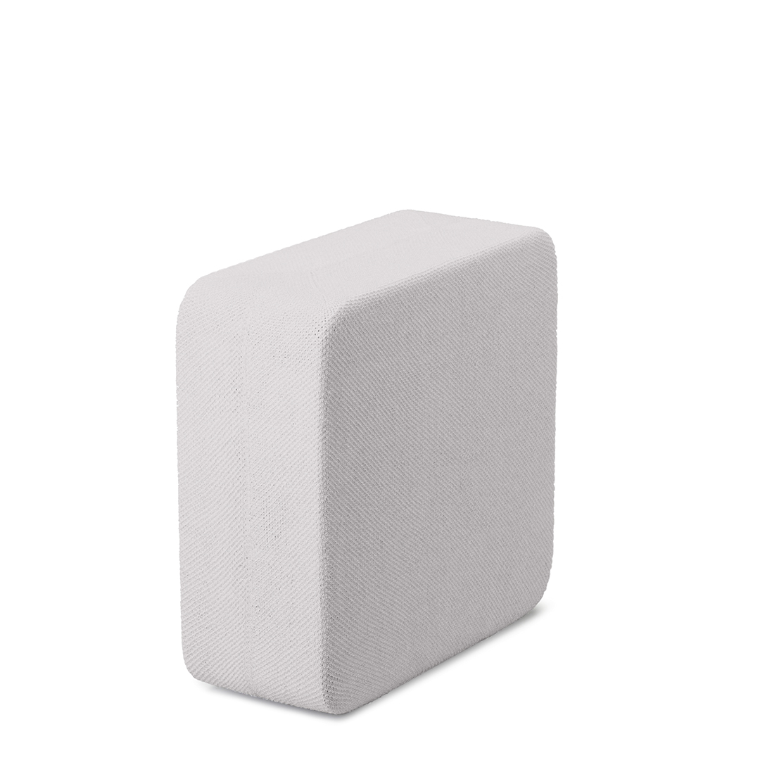 Un objet blanc rectangulaire aux bords arrondis, peut-être un coussin ou un bloc, sur fond blanc, éclairé latéralement.