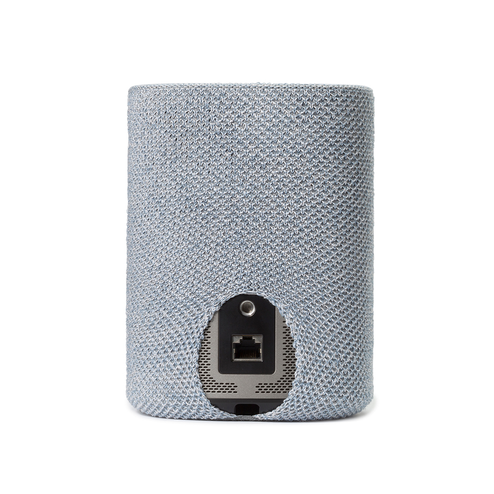 Appareil cylindrique recouvert d'un tissu en maille bleu clair. Une ouverture rectangulaire révèle des ports et connecteurs à l'arrière.