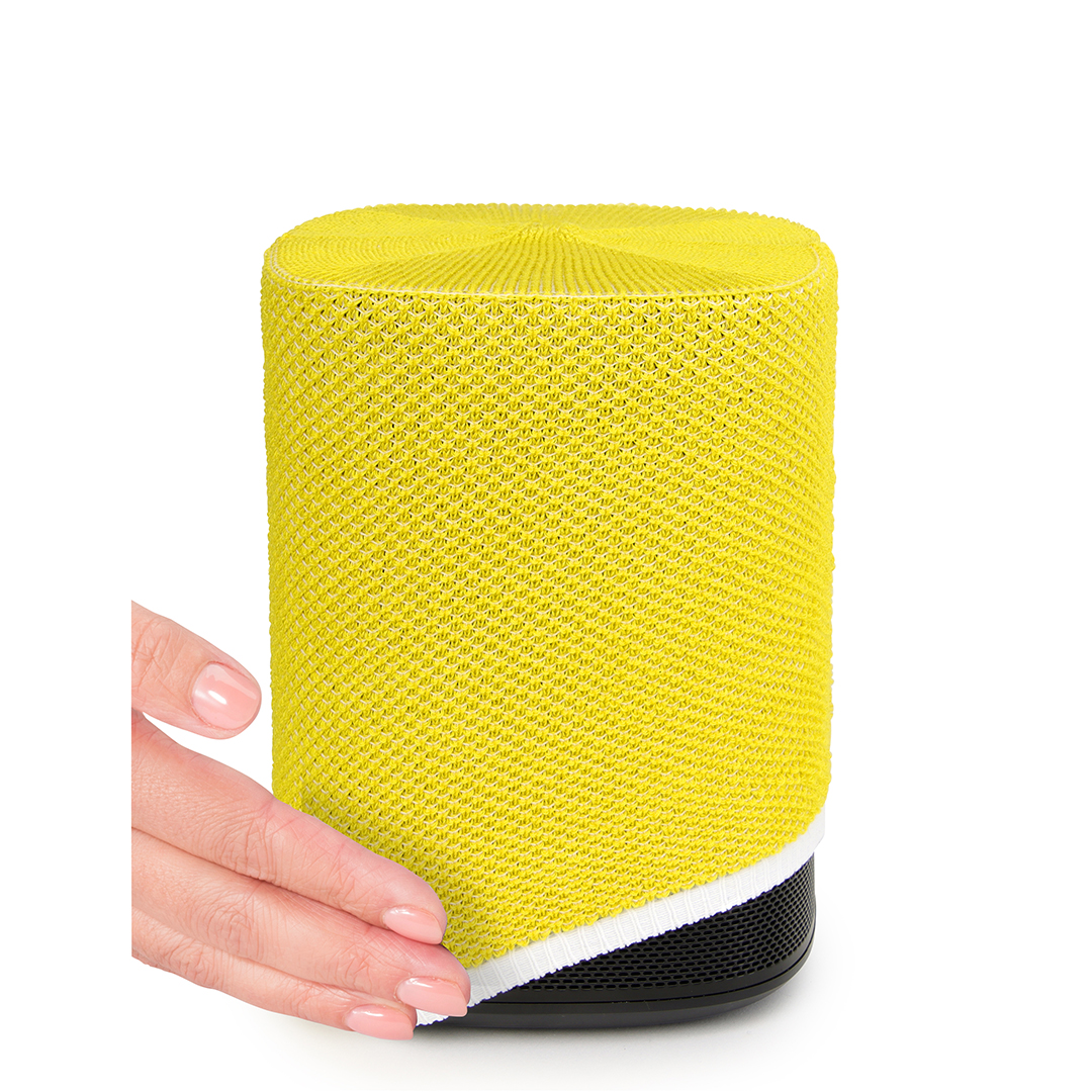 Une main touche un haut-parleur cylindrique jaune. Il a une base noire avec une bordure blanche. Le haut-parleur est sur fond blanc.