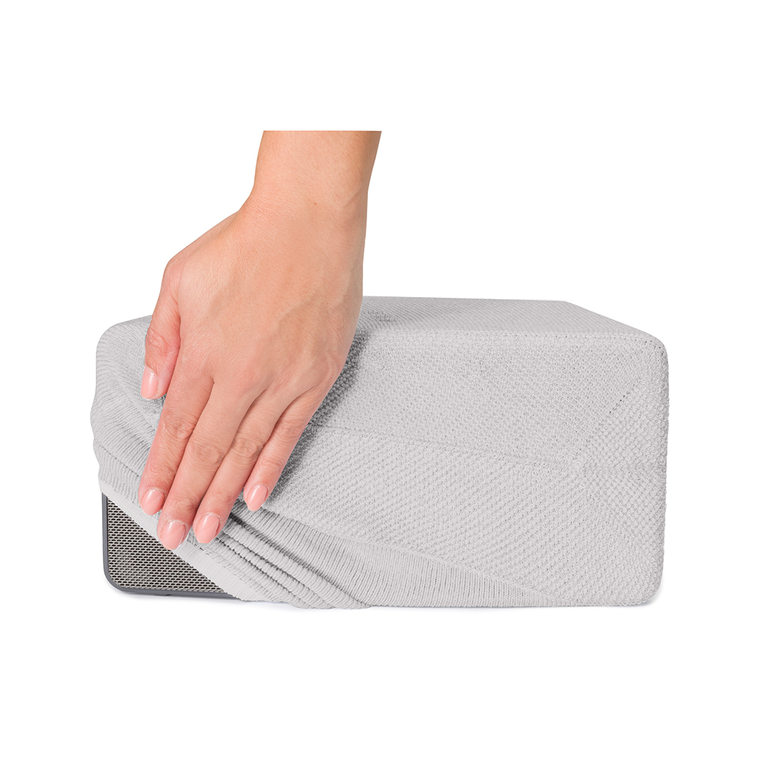Une main lisse une housse en tricot gris clair sur un objet rectangulaire. L'objet a un panneau en mesh.