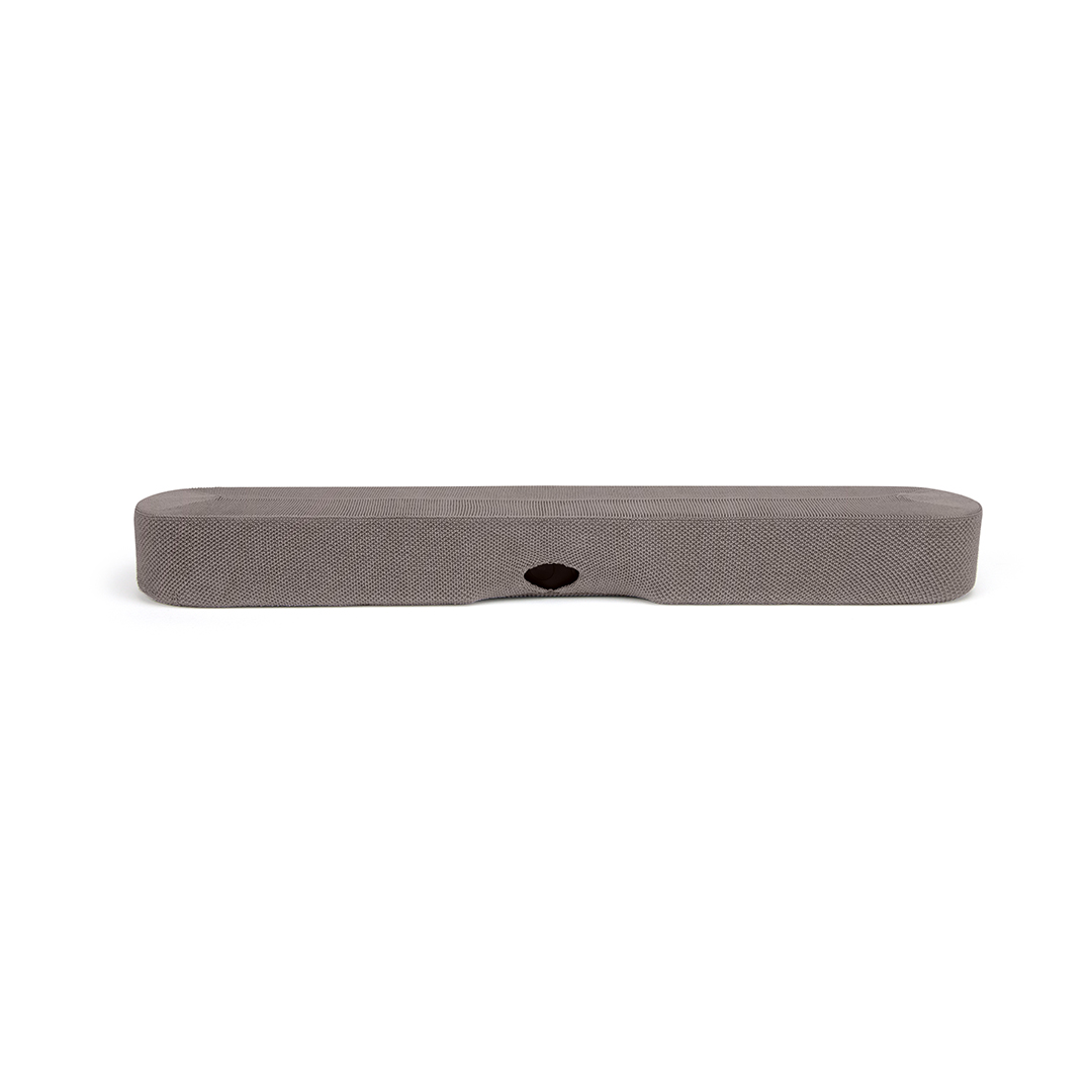 Une barre de son rectangulaire grise est centrée sur un fond blanc. Elle présente une surface texturée, des bords arrondis et un port circulaire sombre.