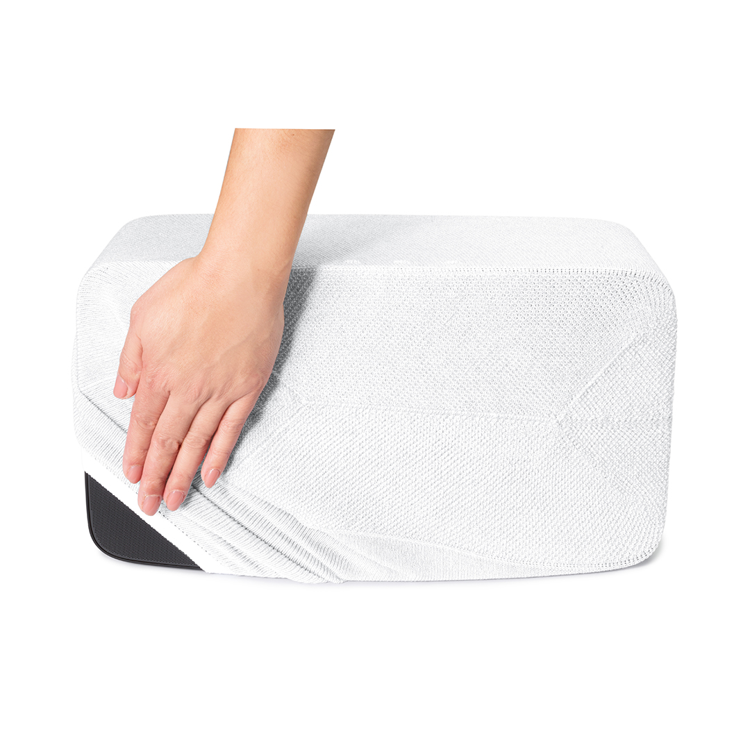 Une main soulève une housse en tissu blanc d'un objet rectangulaire à base noire, révélant une partie de l'objet.