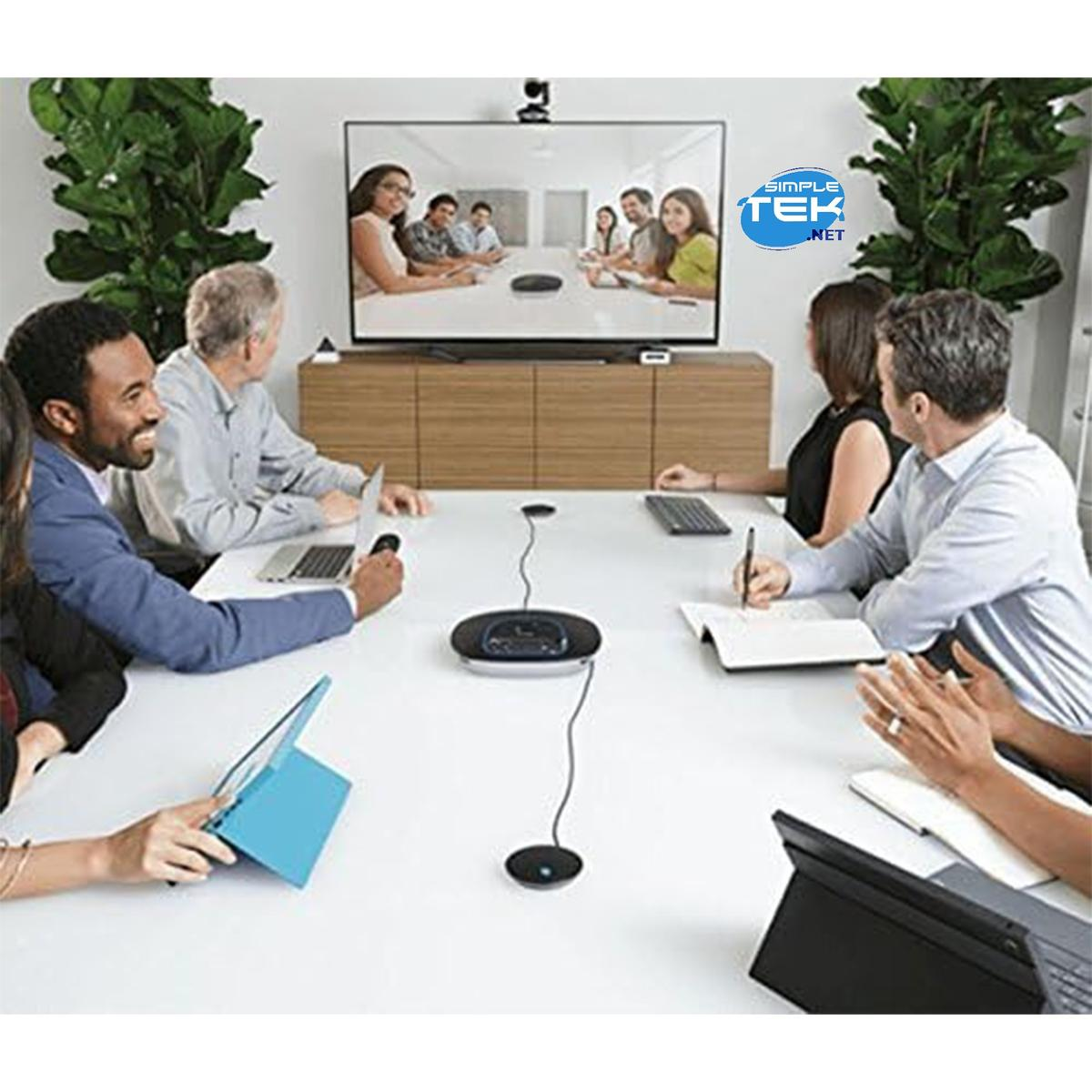 Una sala de reuniones con gente alrededor de una mesa. Una pantalla muestra una videollamada. Todos usan computadoras portátiles y cuadernos.
