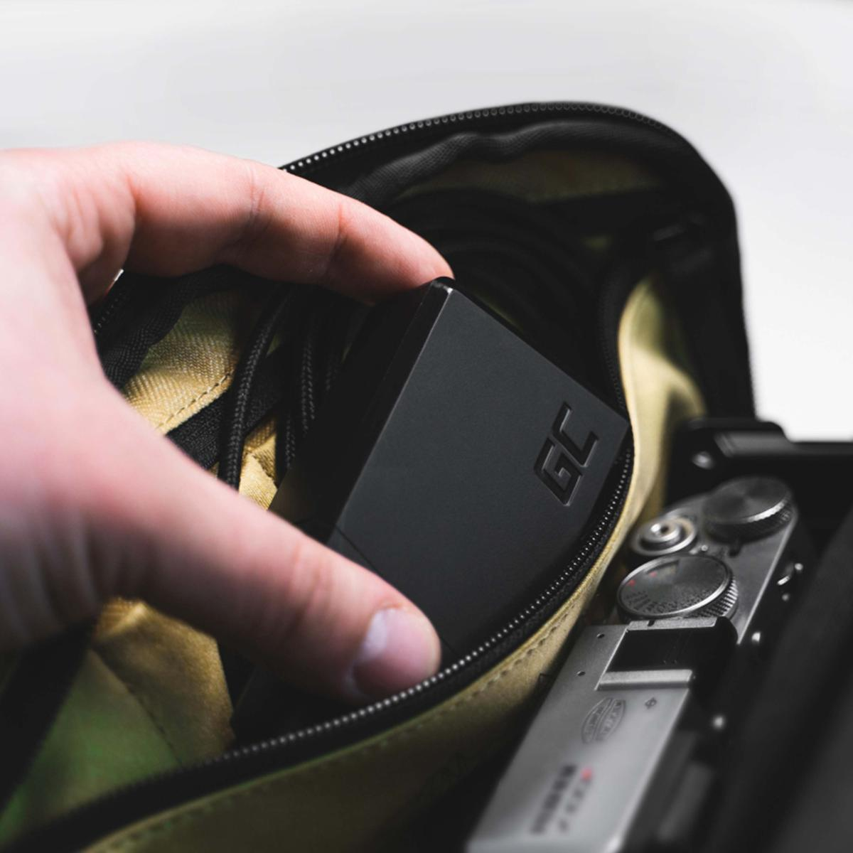 Una mano sostiene un objeto rectangular negro con 'GC' dentro de una bolsa junto a una cámara.