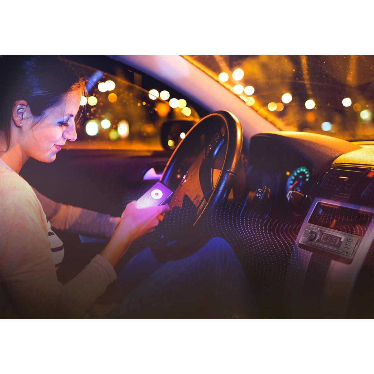 Donna in auto di notte, usa il telefono. Volante, cruscotto visibili. Luci della città sullo sfondo.