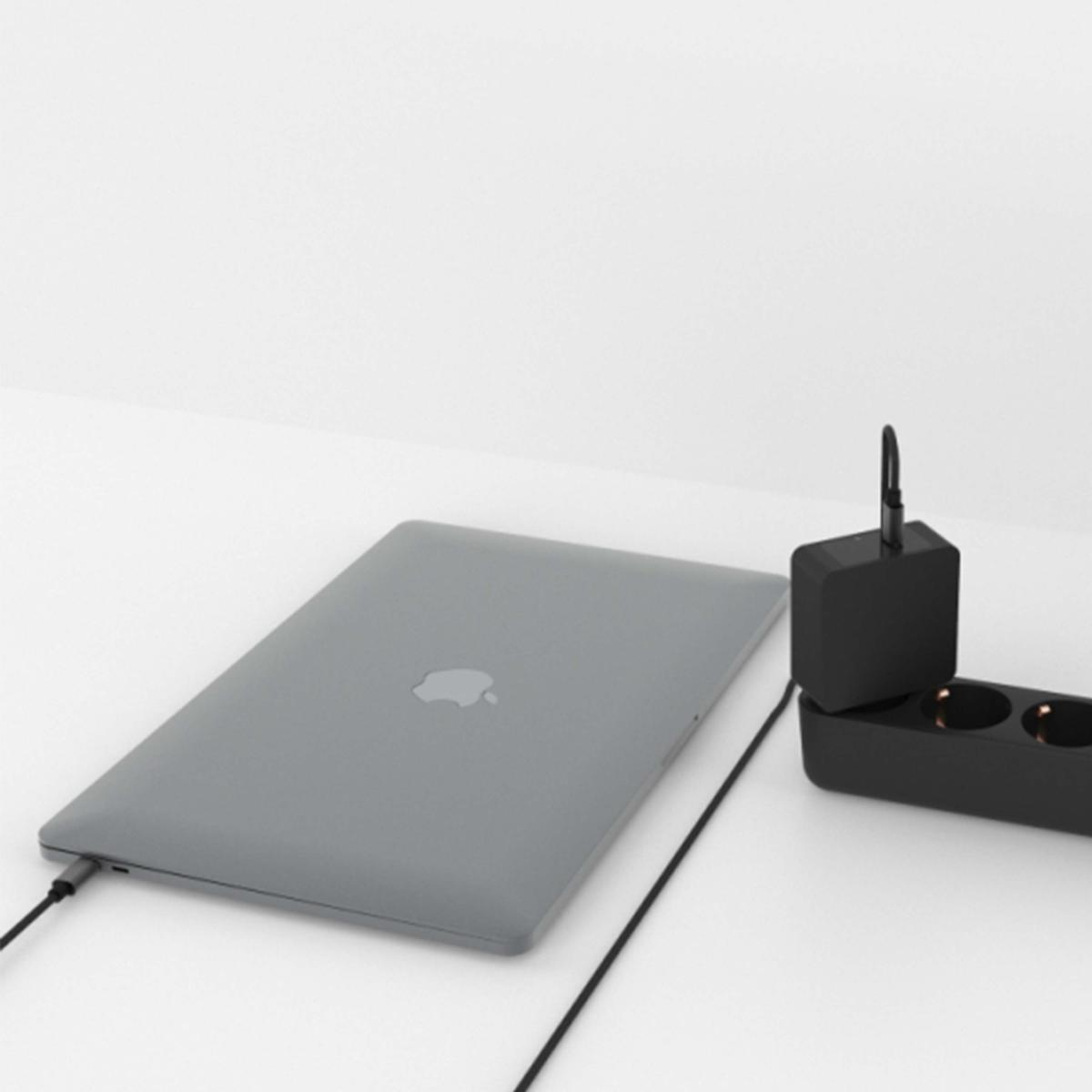 Un MacBook grigio è su una superficie bianca. A destra una ciabatta nera e un caricabatterie. Un cavo collega il laptop.