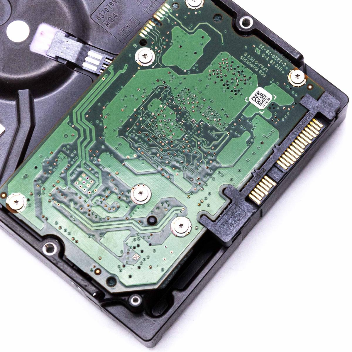 Un circuito stampato verde con motivi intricati è montato su un disco rigido nero. Le viti lo fissano. Connettori visibili.