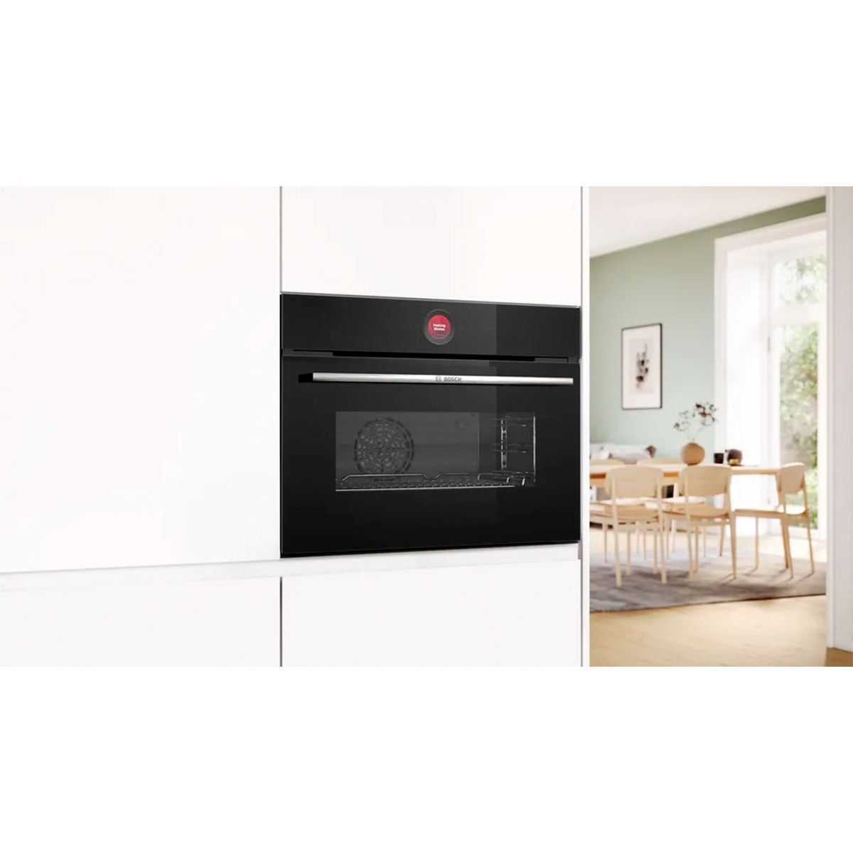 Een zwarte oven is ingebouwd in een witte kast. De ovendeur is van glas. Op de achtergrond een eetkamer met tafel en stoelen.