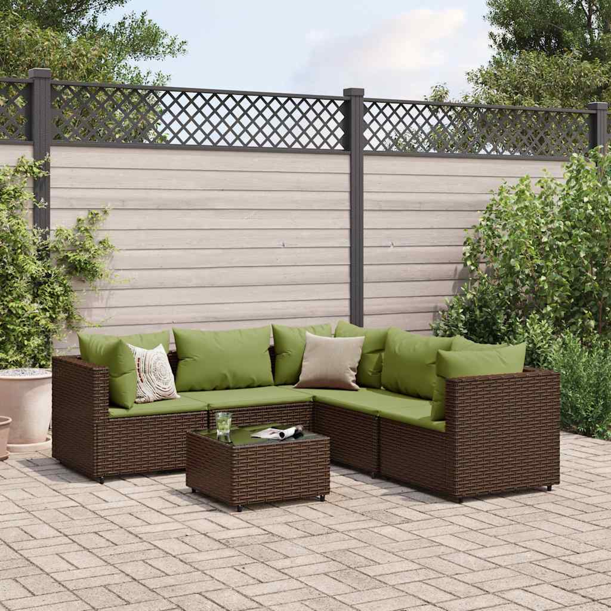 Set da patio esterno con mobili in vimini marrone, cuscini verdi e un tavolino. Sfondo: recinzione in legno e vegetazione.