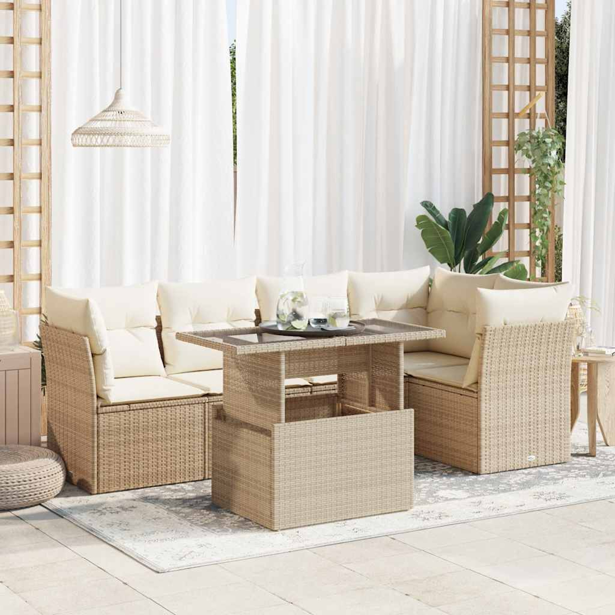 Set di sedute per esterni con tavolo intrecciato, cuscini e tende bianche sullo sfondo. Sono visibili piante e una lampada a sospensione.
