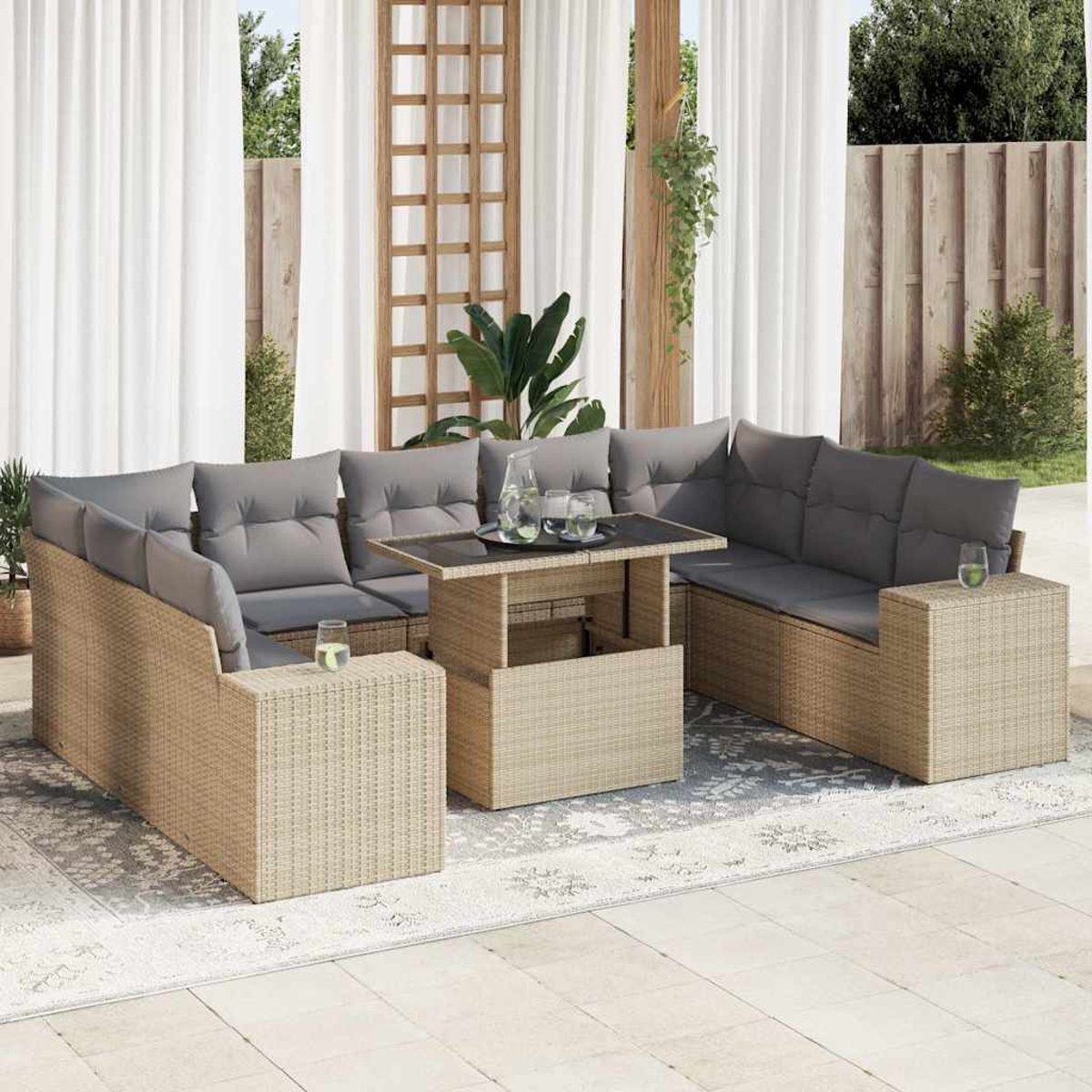 Set di sedute da esterno con struttura in vimini beige e cuscini grigi, include un tavolo con bicchieri, su un tappeto fantasia.