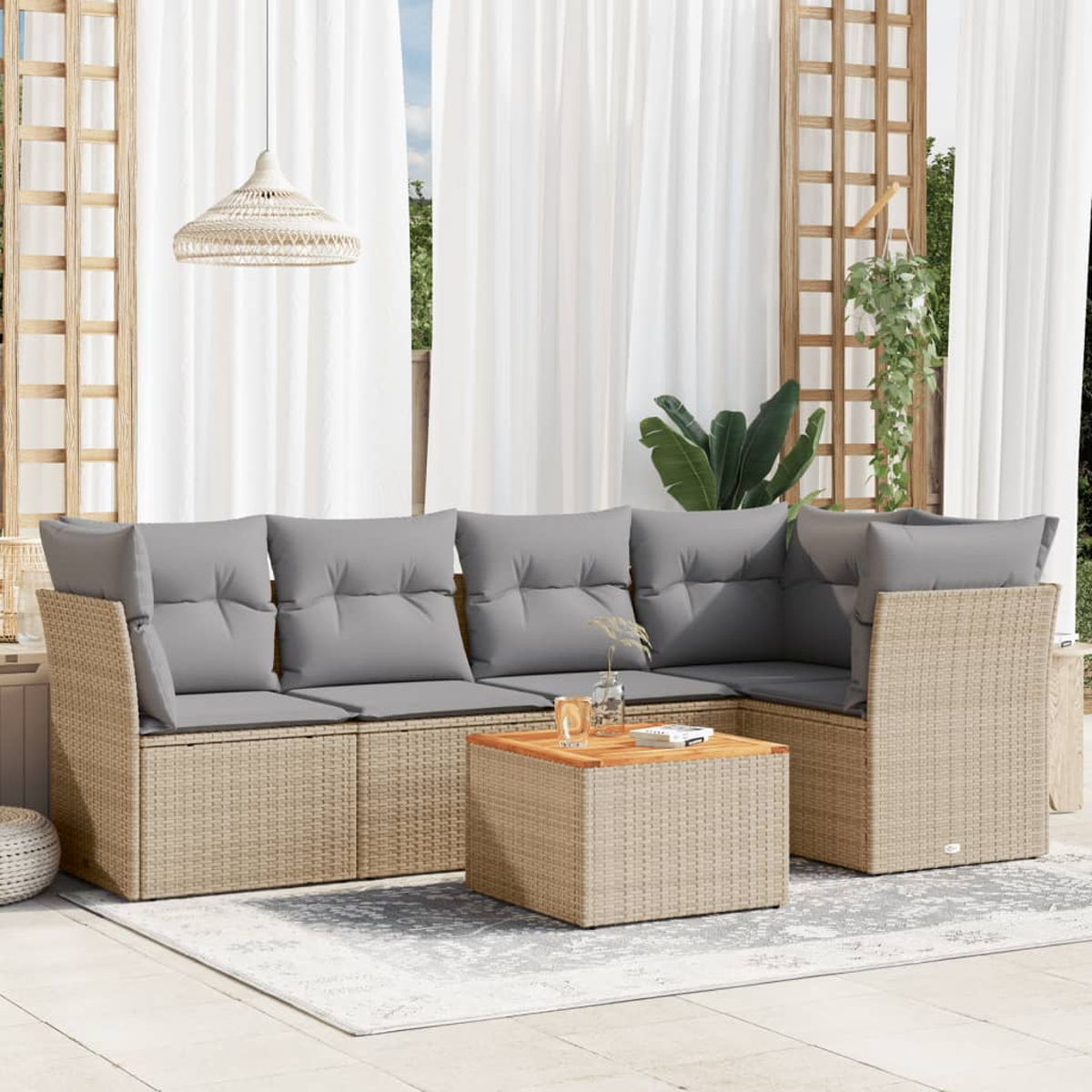 Ein Terrassenset mit grauen Kissen, einem Holztisch und einem gewebten Untergestell. Weiße Vorhänge und eine Hängelampe im Hintergrund.