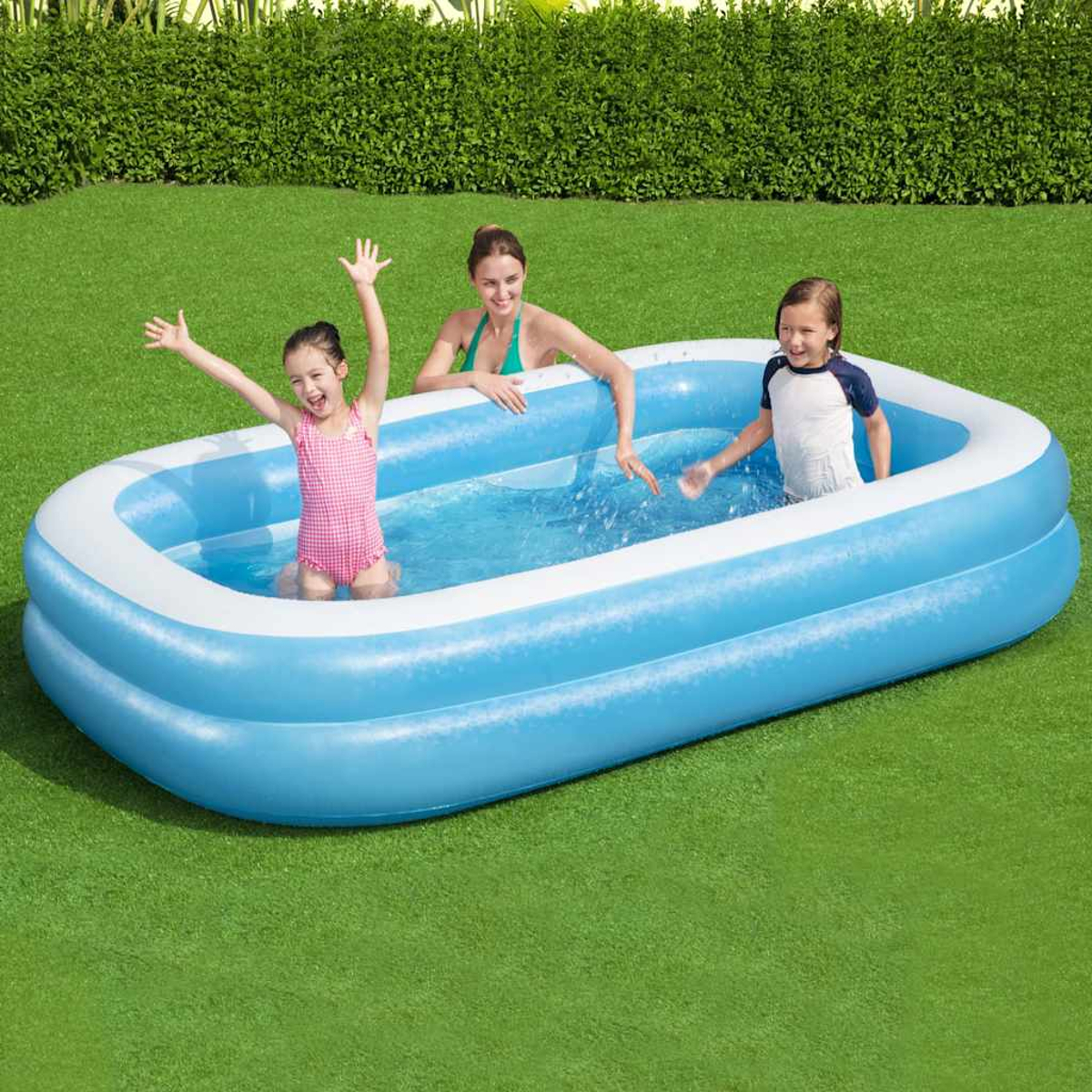 Drie mensen in een blauw opblaaszwembad op gras. Een meisje in roze badpak heft haar armen op. Een vrouw en een jongen zijn ook in het zwembad.