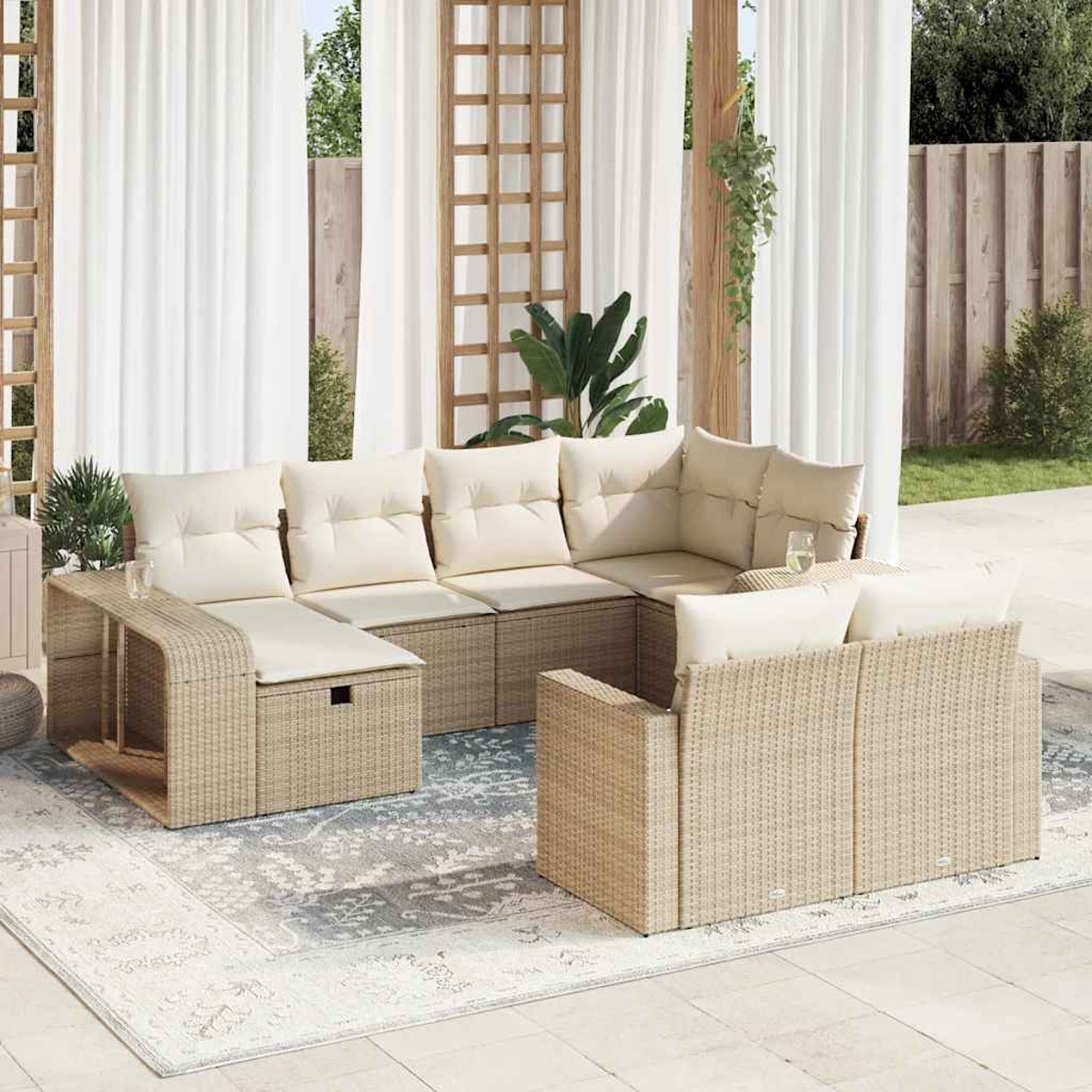 Set di mobili da esterno in vimini con cuscini beige, su un patio con tappeto. Tende bianche e traliccio in legno sullo sfondo.