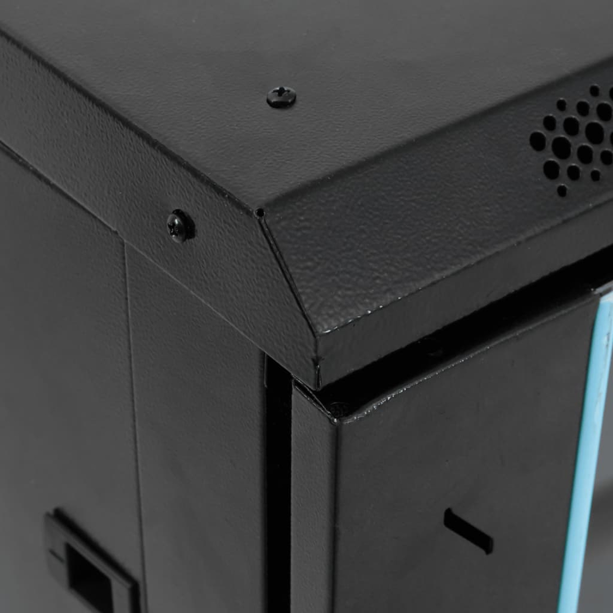 Nahaufnahme einer schwarzen Metallbox. Ecken, Schrauben und Lüftungslöcher sind sichtbar. Die Box hat eine matte Oberfläche.