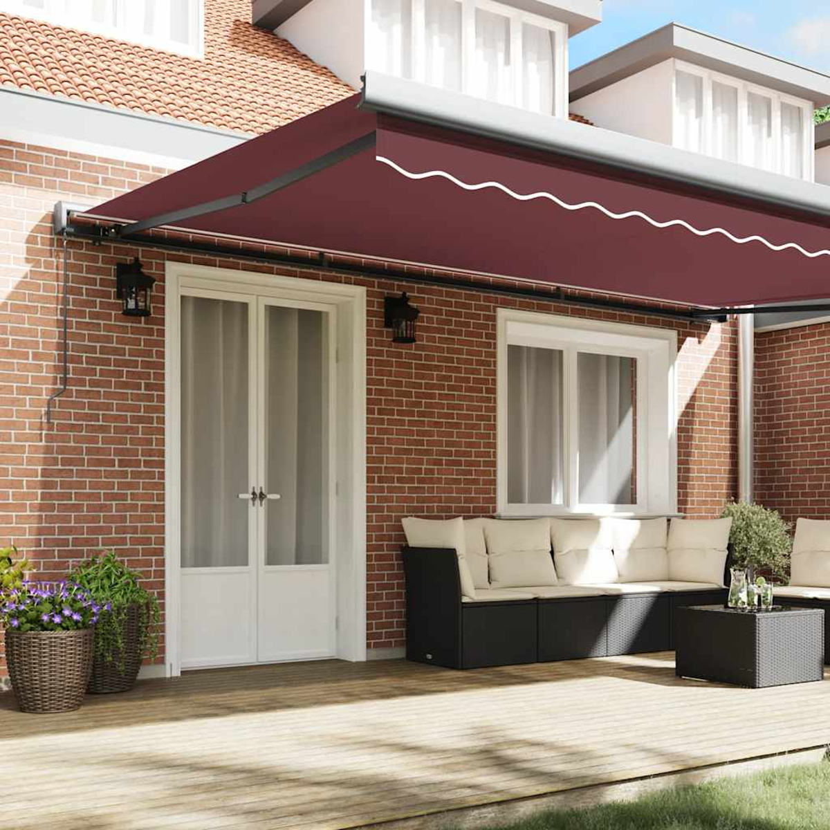 Un patio con tenda da sole rossa, porte bianche e divano nero. Piante in vaso sul terrazzo in legno. Muro di mattoni e cielo blu.