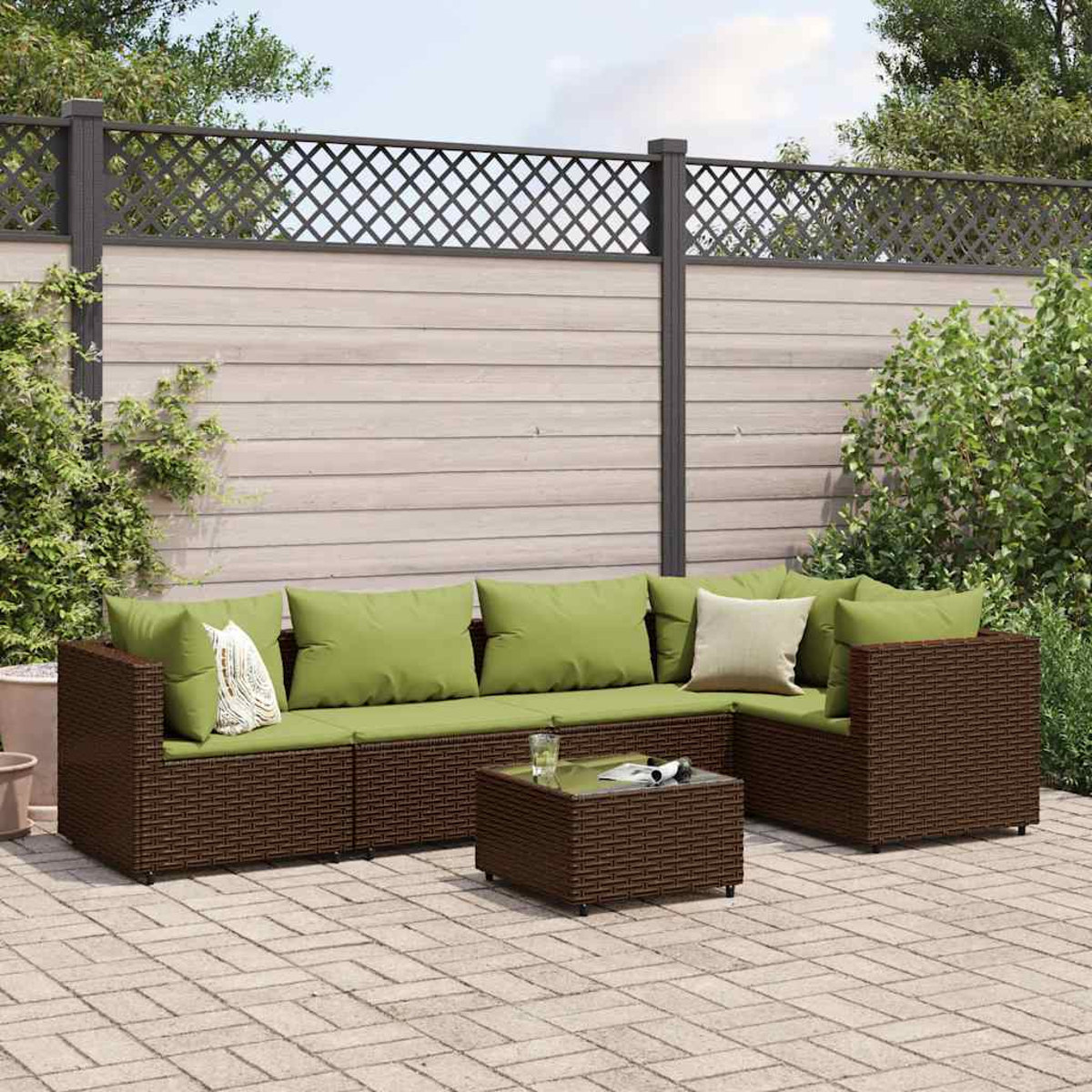 Un set da patio esterno con mobili in vimini marrone e cuscini verdi. Un tavolino da caffè con piano in vetro si trova di fronte. Una recinzione sullo sfondo.
