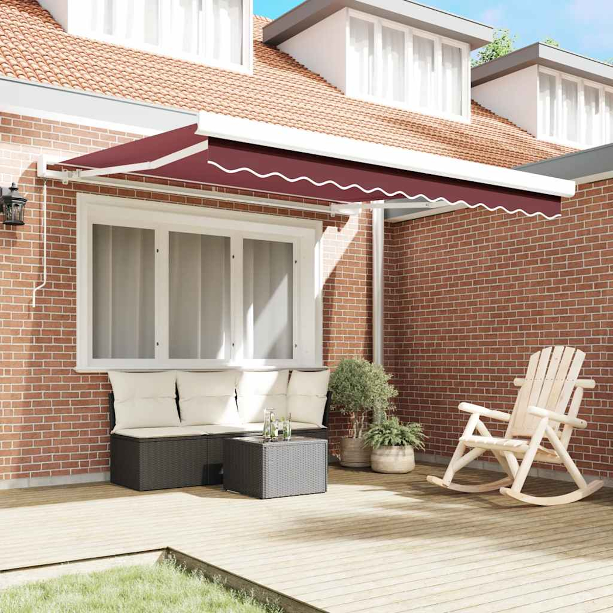 Ein Haus mit roter Backsteinmauer und Holzterrasse. Es gibt eine weinrote Markise, eine Bank, einen Schaukelstuhl und Pflanzen.