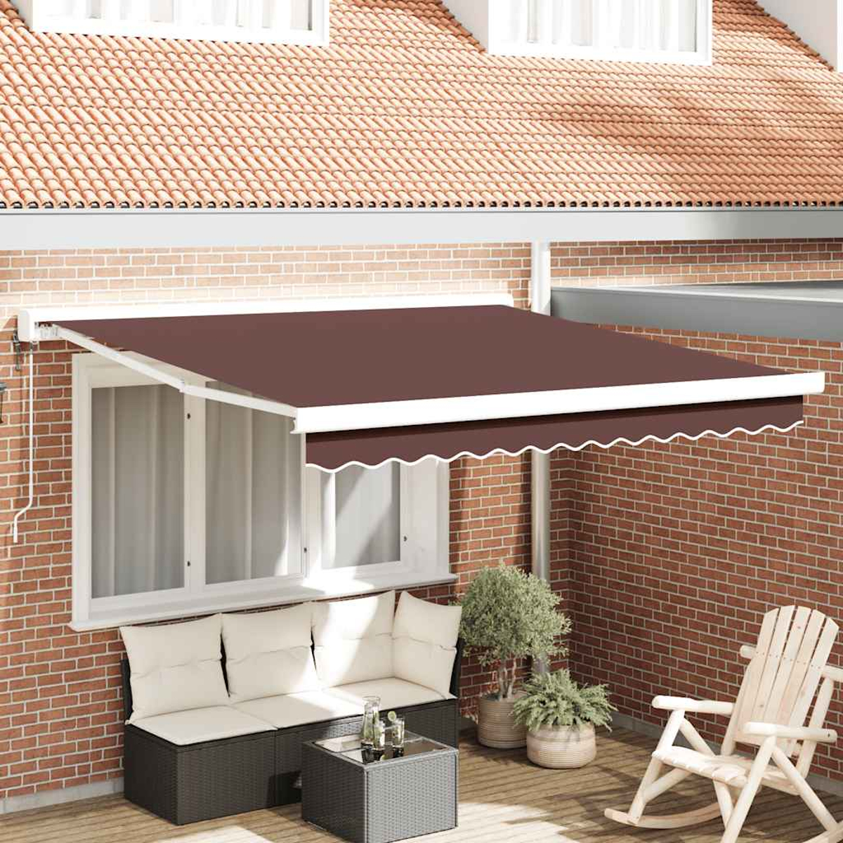 Una tenda da sole marrone ombreggia un patio con un divano, piante e una sedia a dondolo. Muro di mattoni rossi e tetto di tegole sullo sfondo.