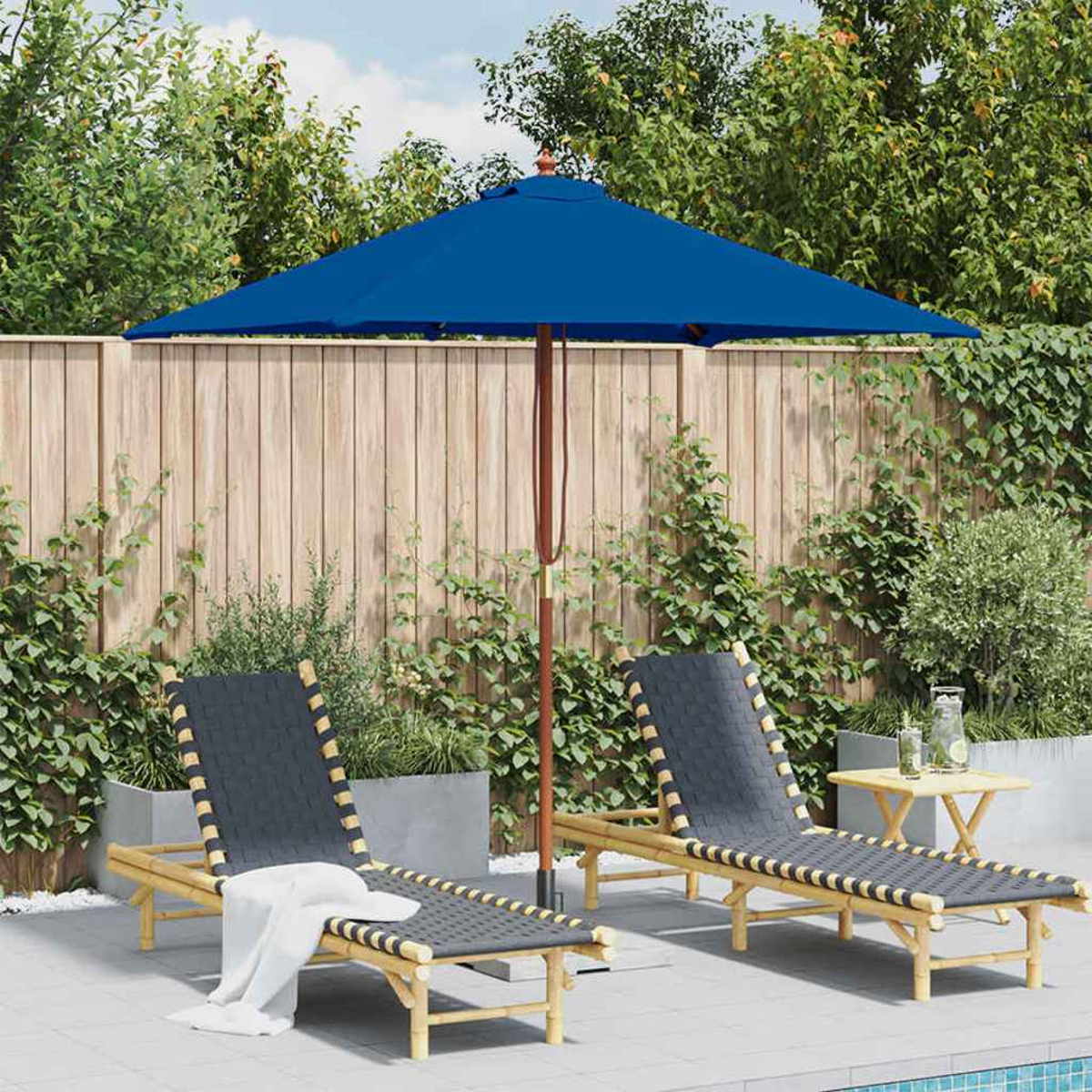 Zwei Liegestühle mit blauem Sonnenschirm. Holzzaun und Grün im Hintergrund. Kleiner Tisch und Pool.