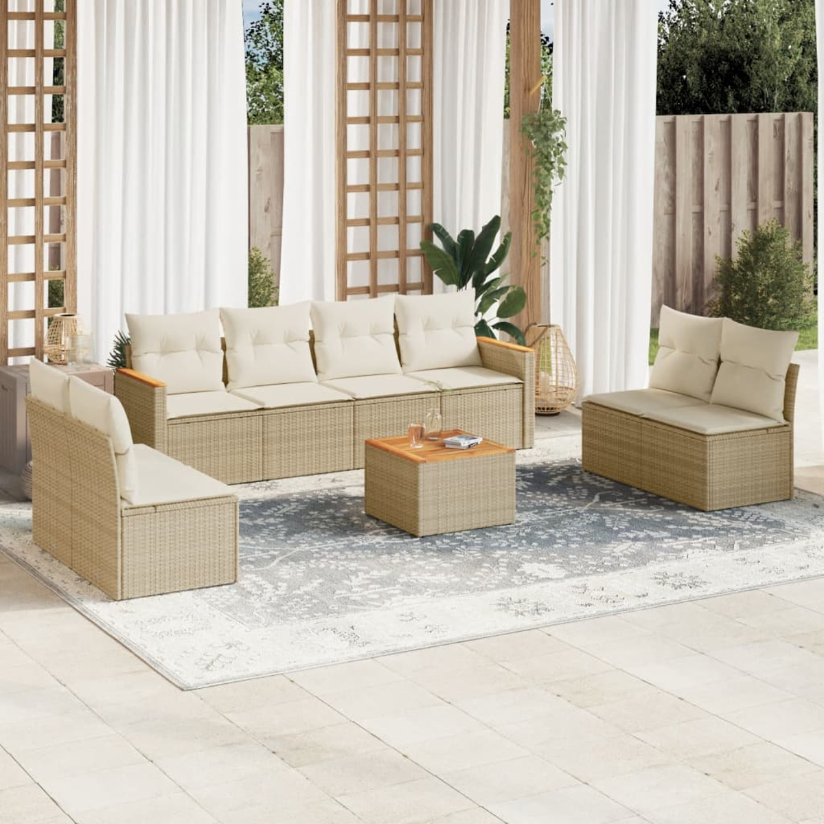 Gartenmöbel-Set. Beiges Korbmöbel-Set auf einem Musterteppich. Vorhänge und Holzgitter im Hintergrund.