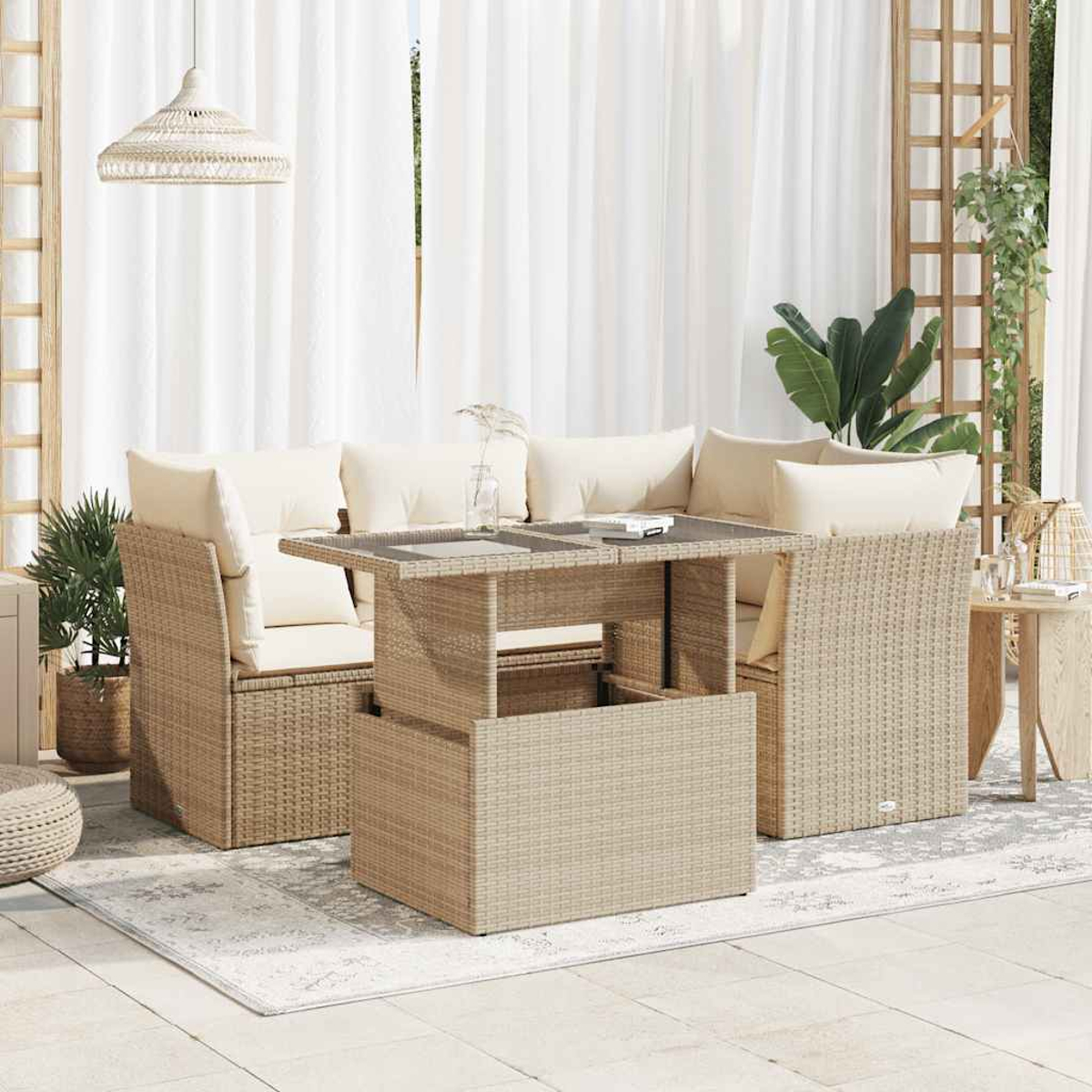 Set di mobili da patio con sedie in stile rattan e un tavolo. Cuscini color crema, tende bianche e piante sullo sfondo.