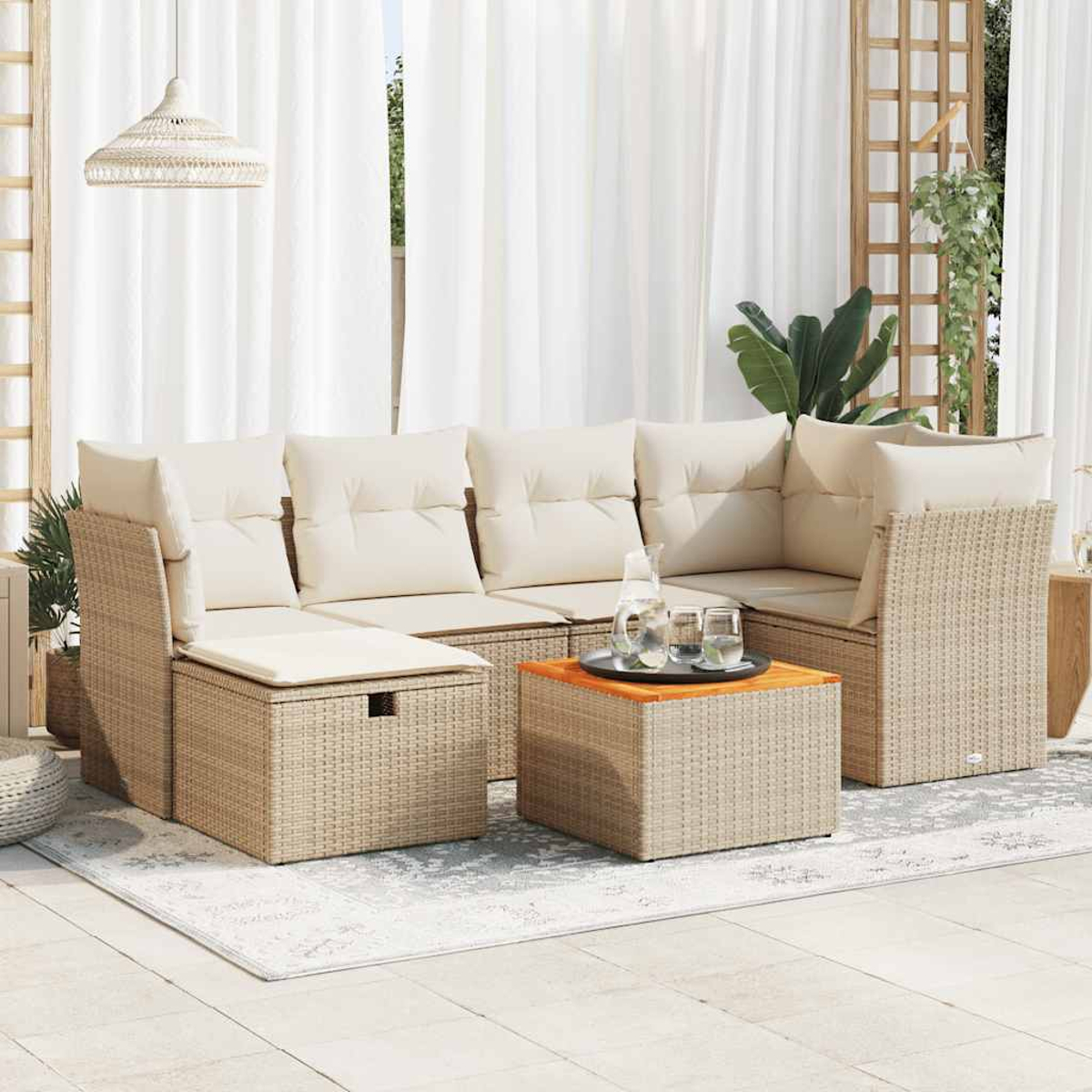 Geflochtenes Outdoor-Ecksofa mit cremefarbenen Kissen und einem kleinen Tisch mit Gläsern und Wasser. Im Hintergrund weiße Vorhänge.