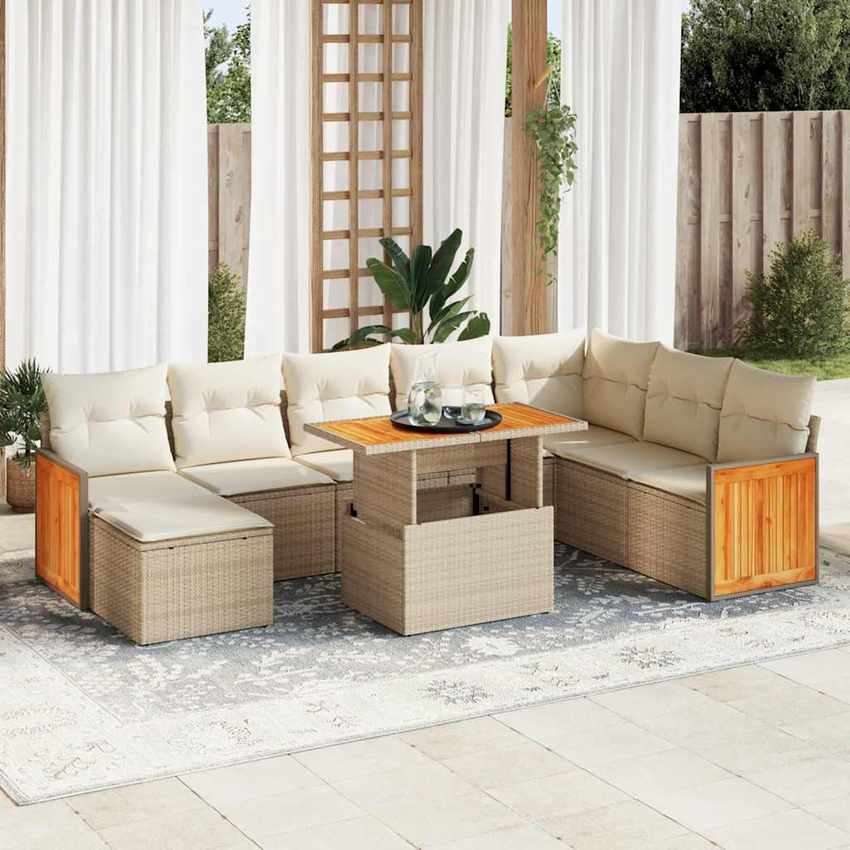 Set da patio all'aperto con cuscini beige, un tavolo di legno e un tappeto fantasia. Lo sfondo mostra tende, alberi e una recinzione.
