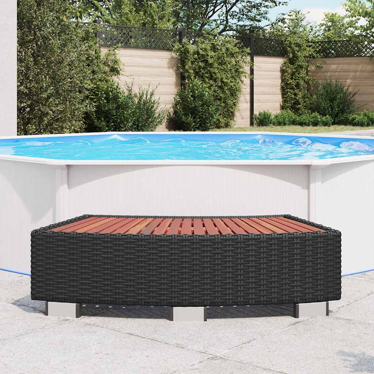 Ein quadratischer, schwarzer Korbtisch mit Holzplatte steht vor einem Pool. Bäume und ein Zaun sind im Hintergrund.